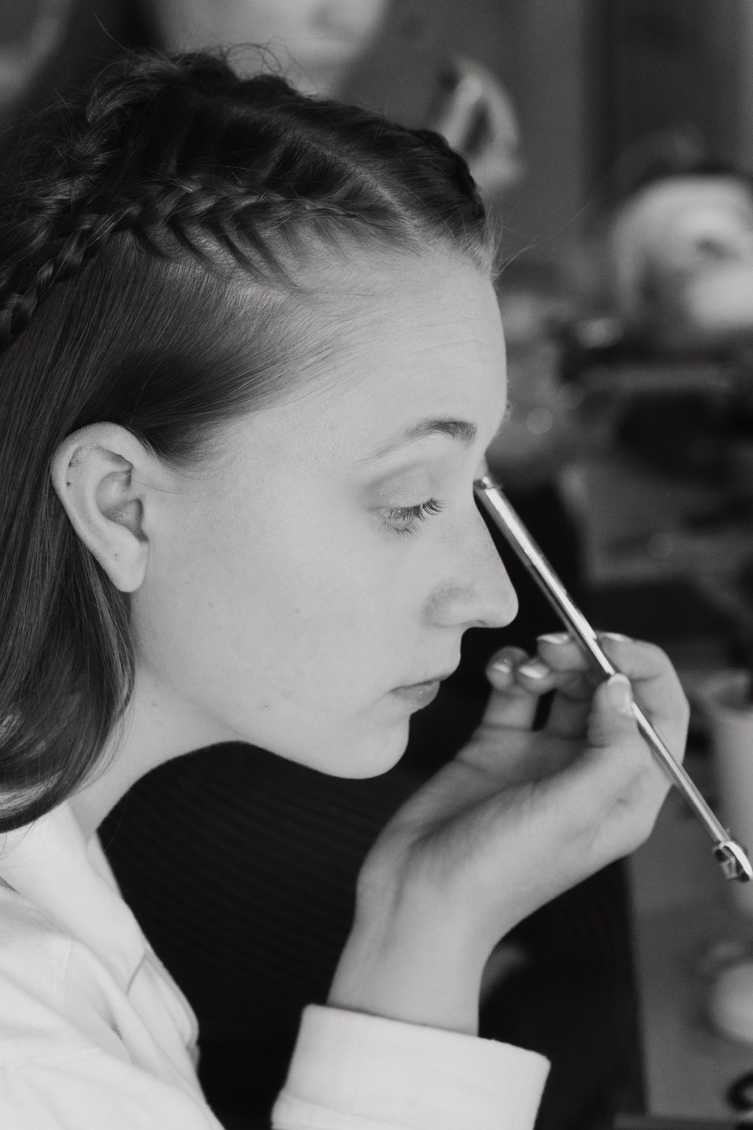 Black and white photo of a bride getting eye makeup applied by a makeup artist before her wedding.