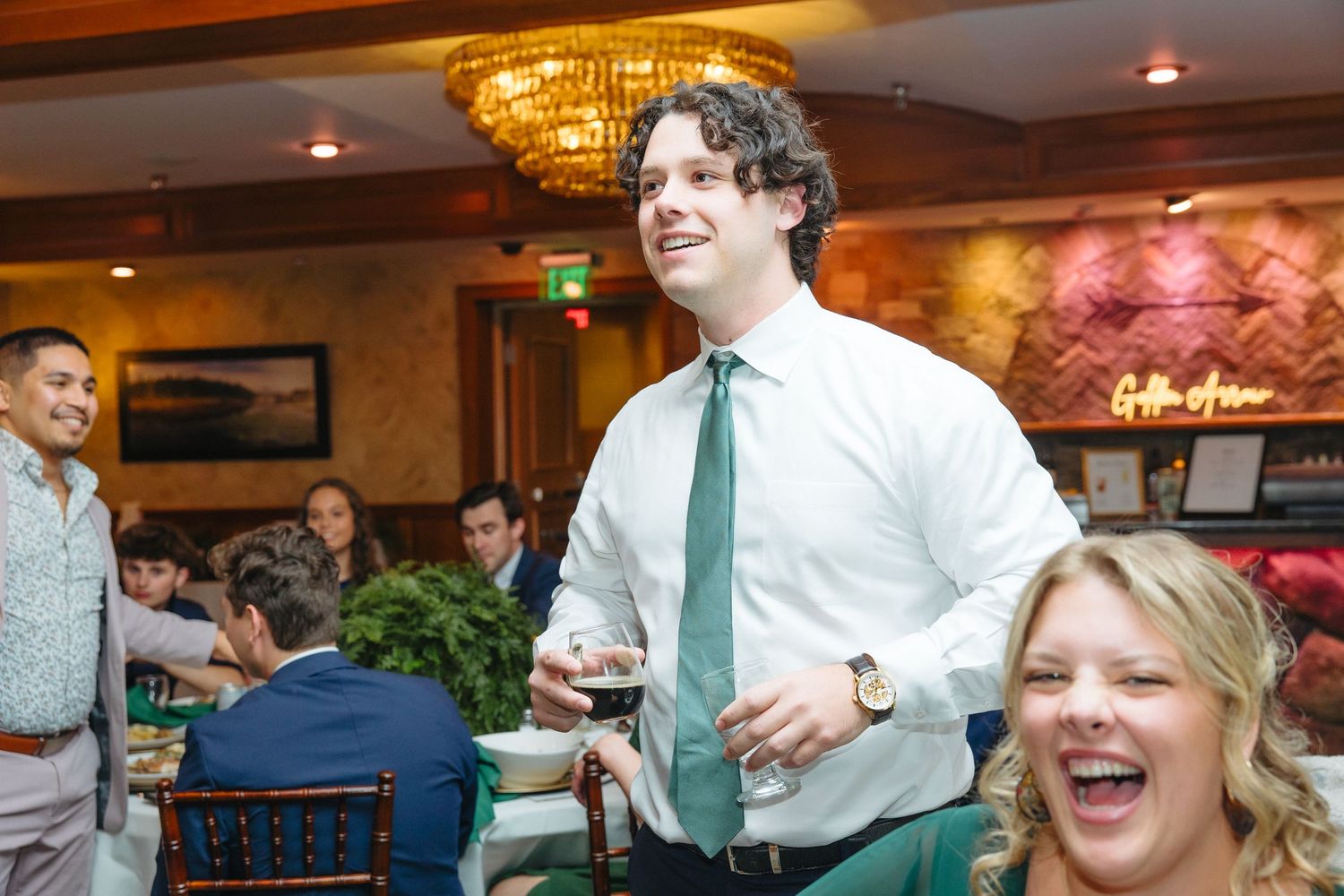 Smiling man in white shirt and green tie mingles with guests at a wedding reception.