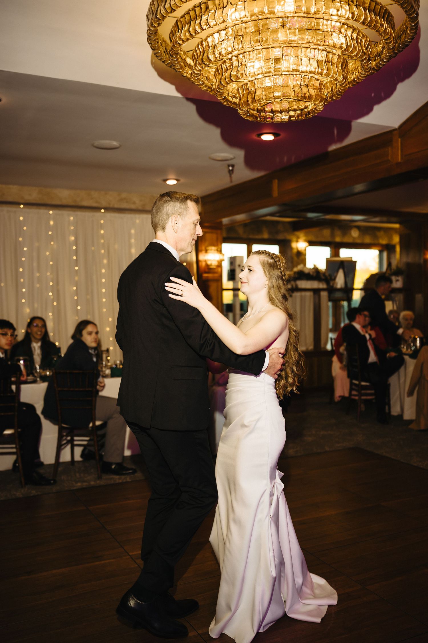 Bride and groom share romantic first dance under golden chandelier at wedding reception.