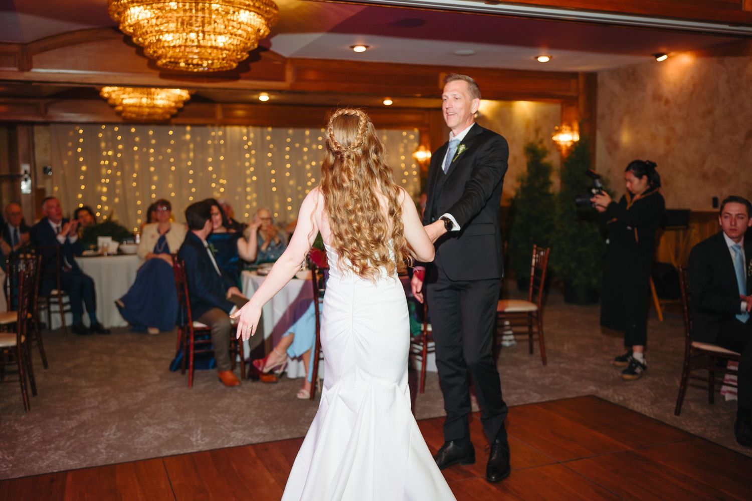 Bride and groom share their first dance in an elegant reception hall with warm lighting and seated guests.