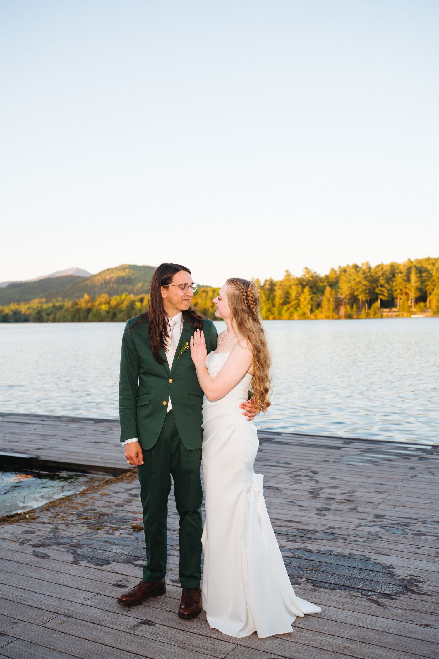 Bride and groom share a romantic moment on a wooden dock at golden hour by a lake.