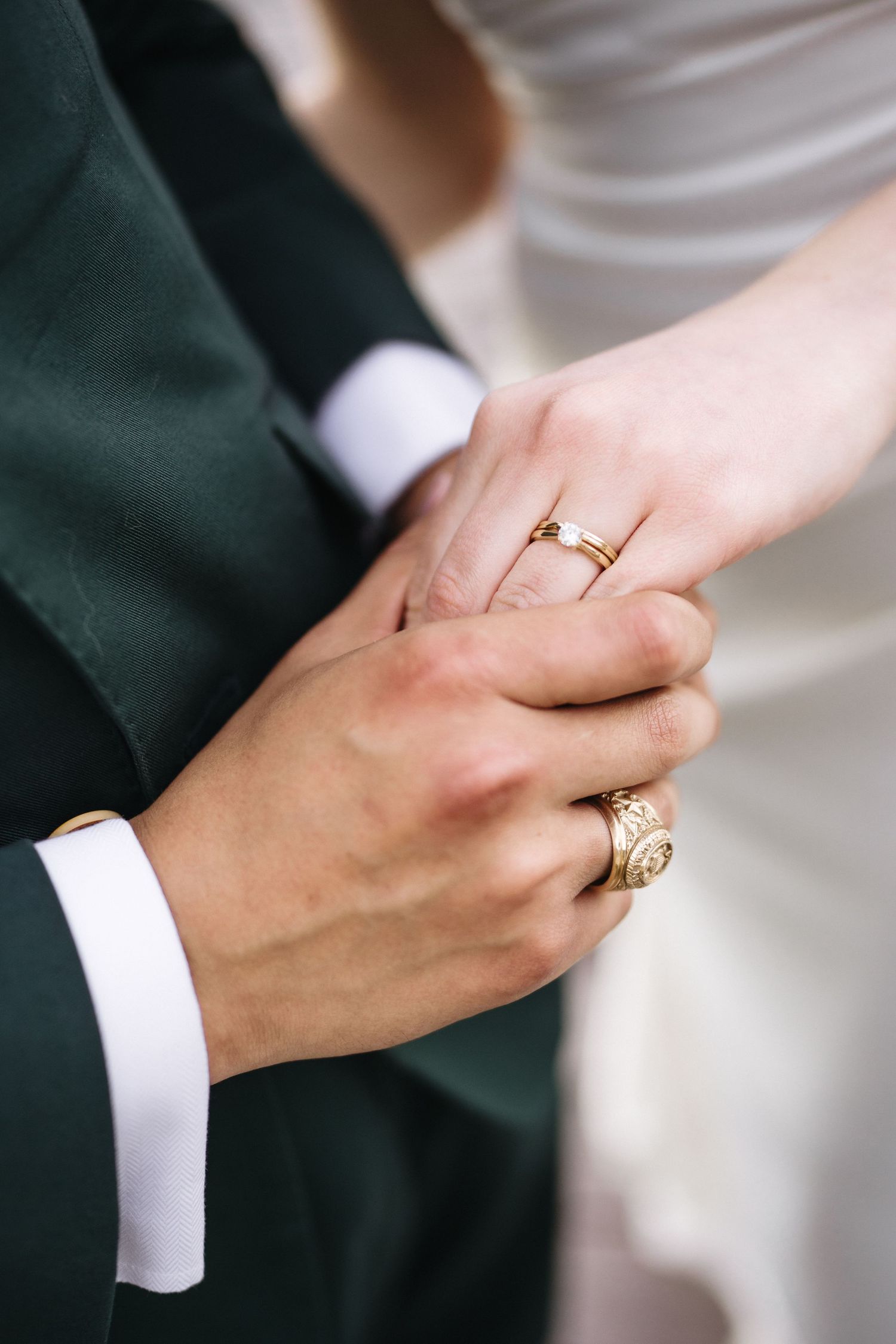 Close-up of newlyweds holding hands showing gold wedding rings and engraved band.