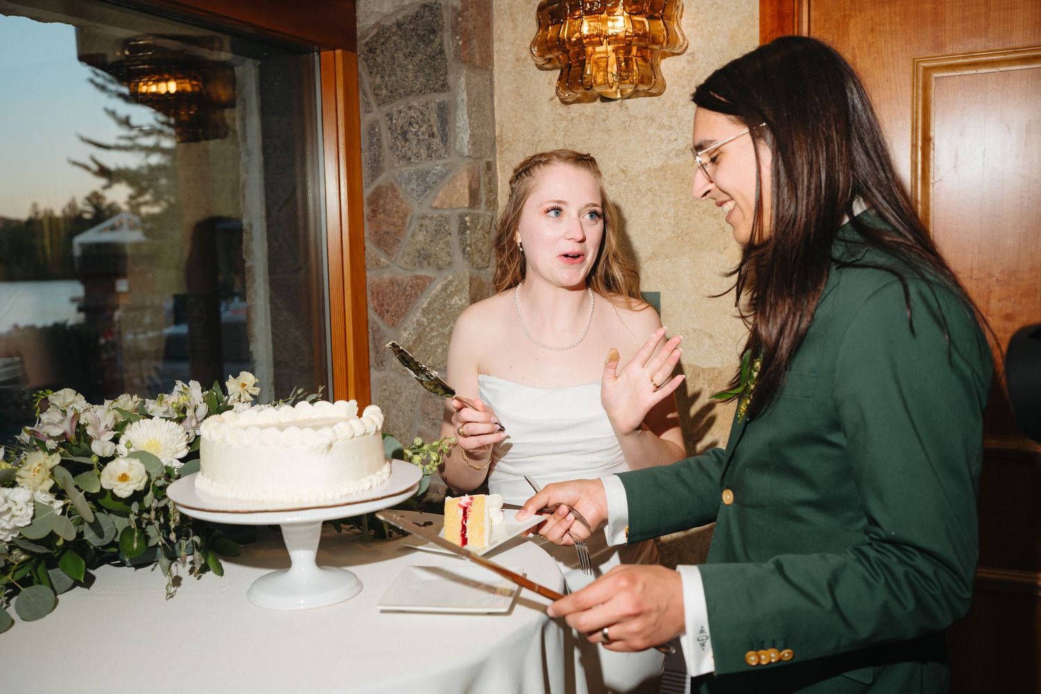 Bride and groom cutting white wedding cake at elegant indoor reception with floral decorations.