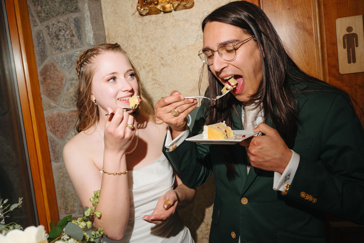 Bride and groom laughing while feeding each other wedding cake at their reception.
