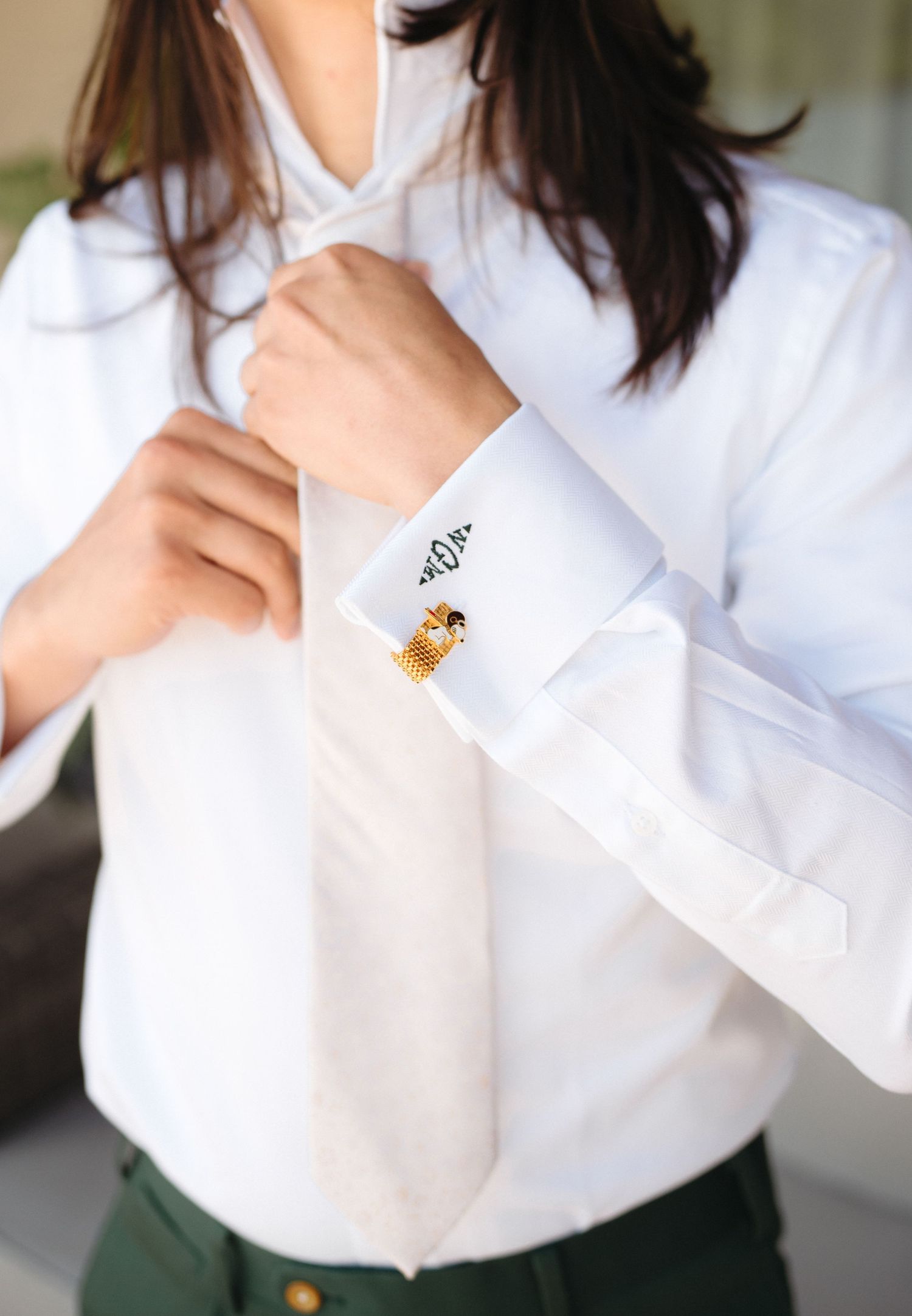 Woman in white dress shirt adjusting collar with gold monogram cufflinks on her wrist.