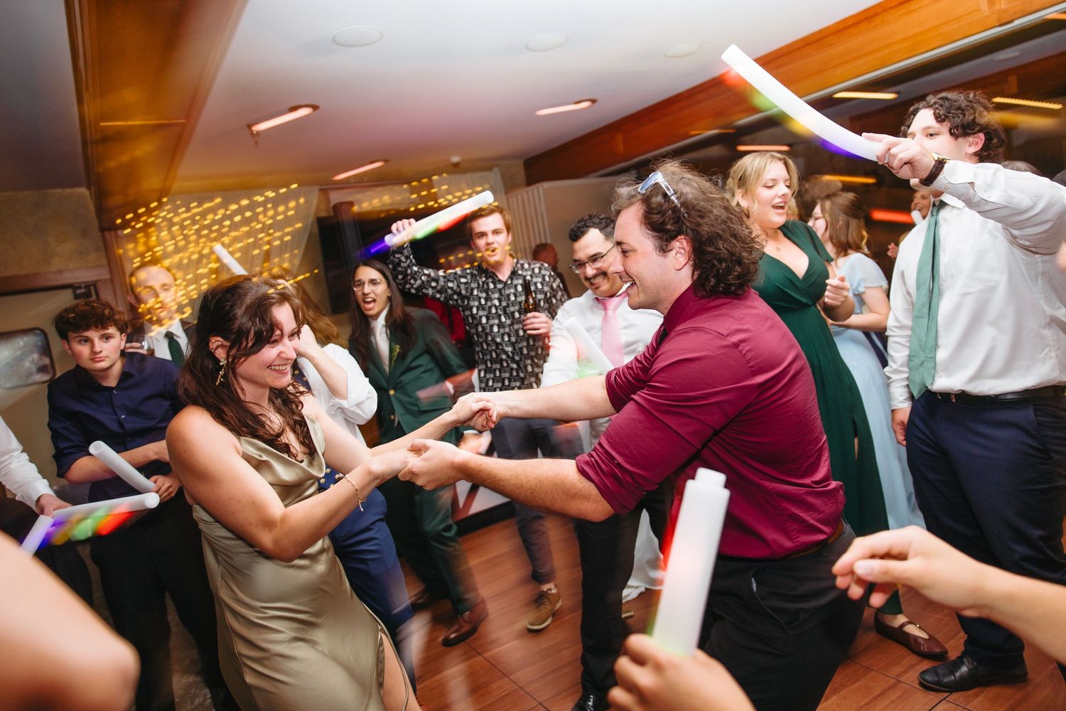 Guests dancing energetically at a wedding reception, holding glow sticks and celebrating on the dance floor.