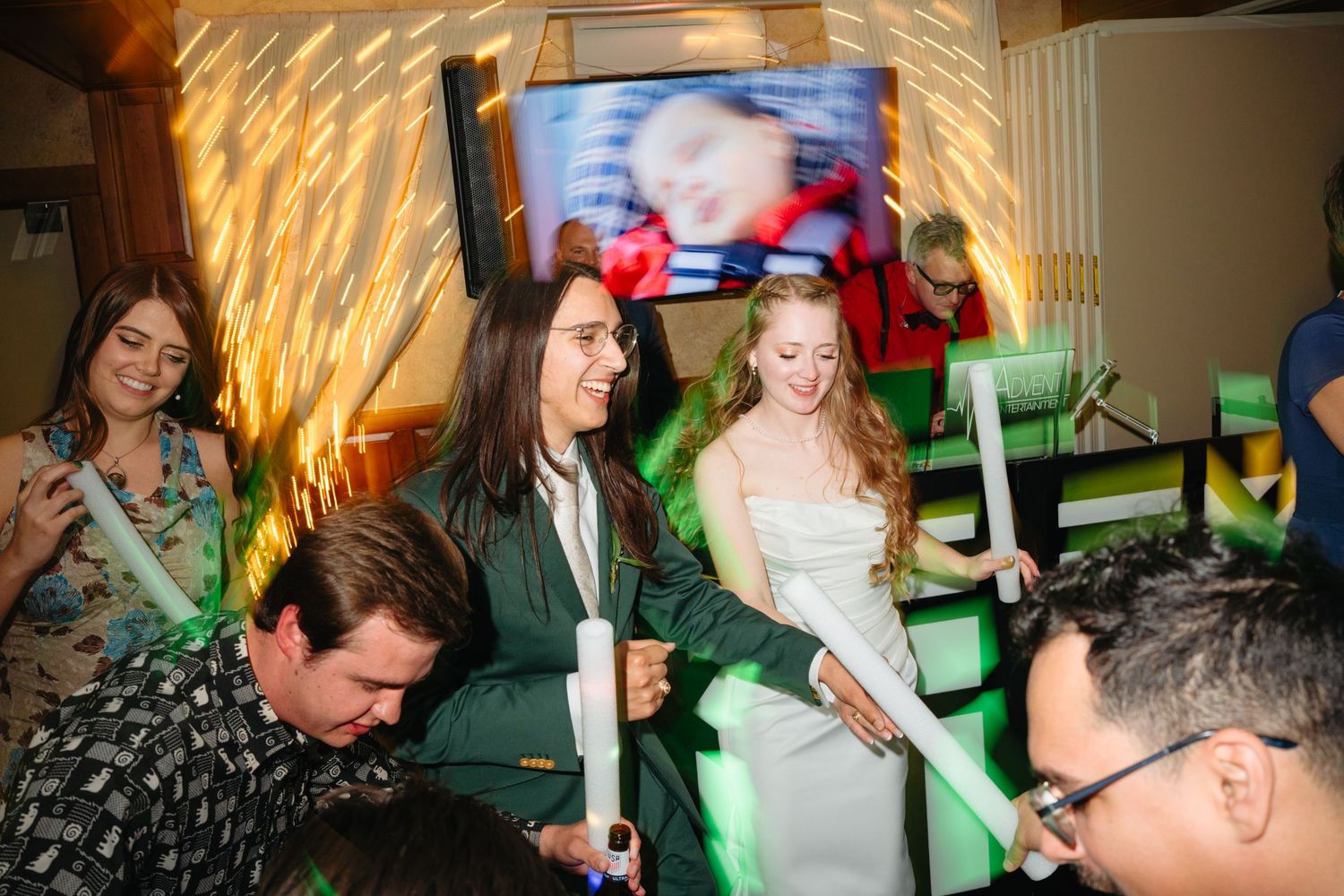Guests dance and celebrate at a lively wedding reception with glowing light sticks and festive decorations.