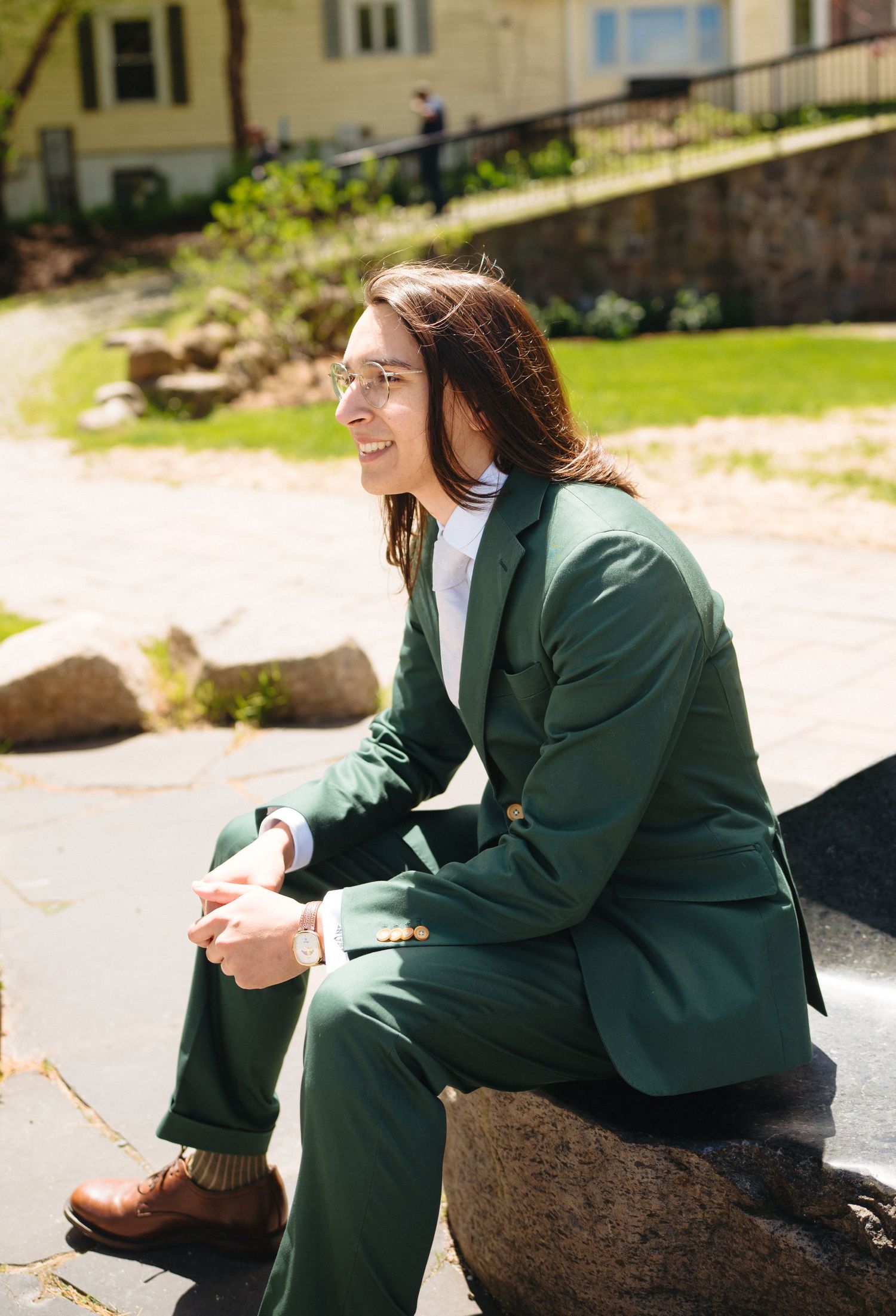 Young person in green suit sitting on a rock outdoors smiling on a sunny spring day.