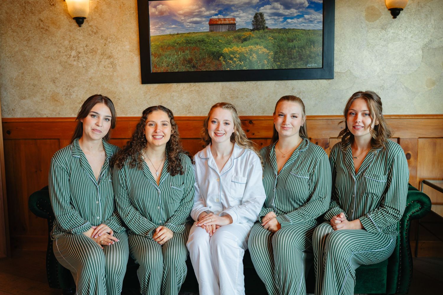 Bride and four bridesmaids wearing matching green striped pajamas sitting together during wedding morning preparations.