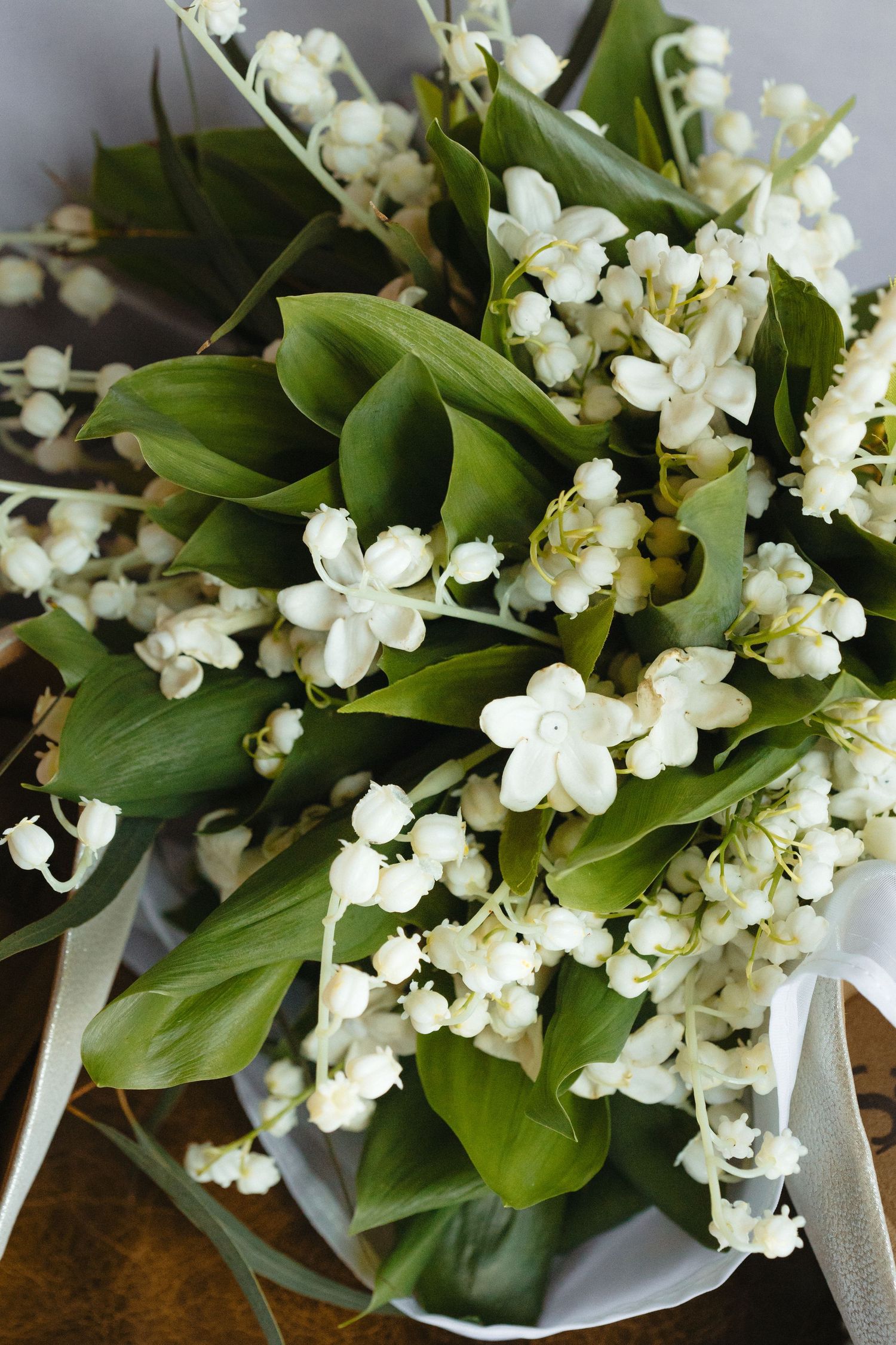 Close-up of a lush bridal bouquet featuring white lily of the valley blooms and green leaves.