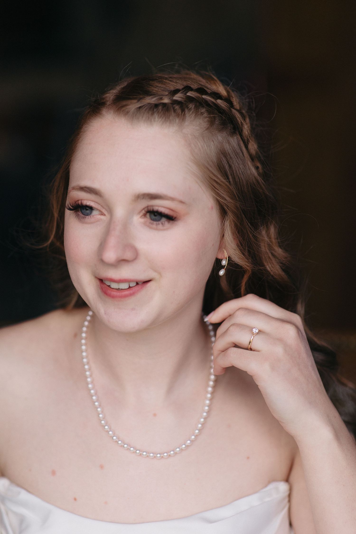 Beautiful bride with braided updo wearing pearl necklace and engagement ring on her wedding day.