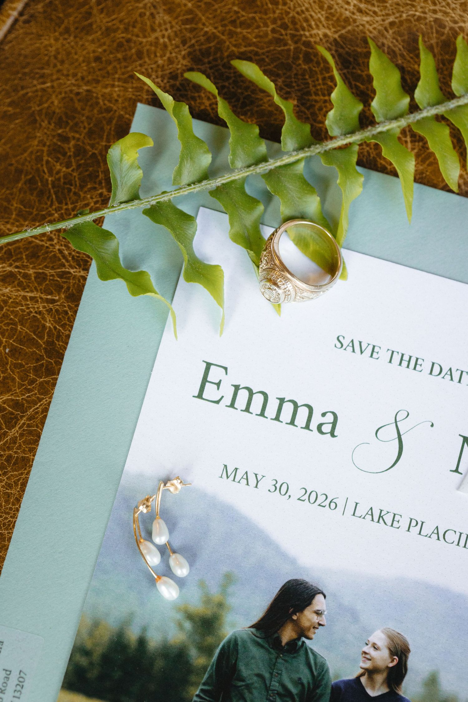 Save the date card for Emma's Lake Placid wedding on May 30 2026, styled with gold ring and fern greenery.