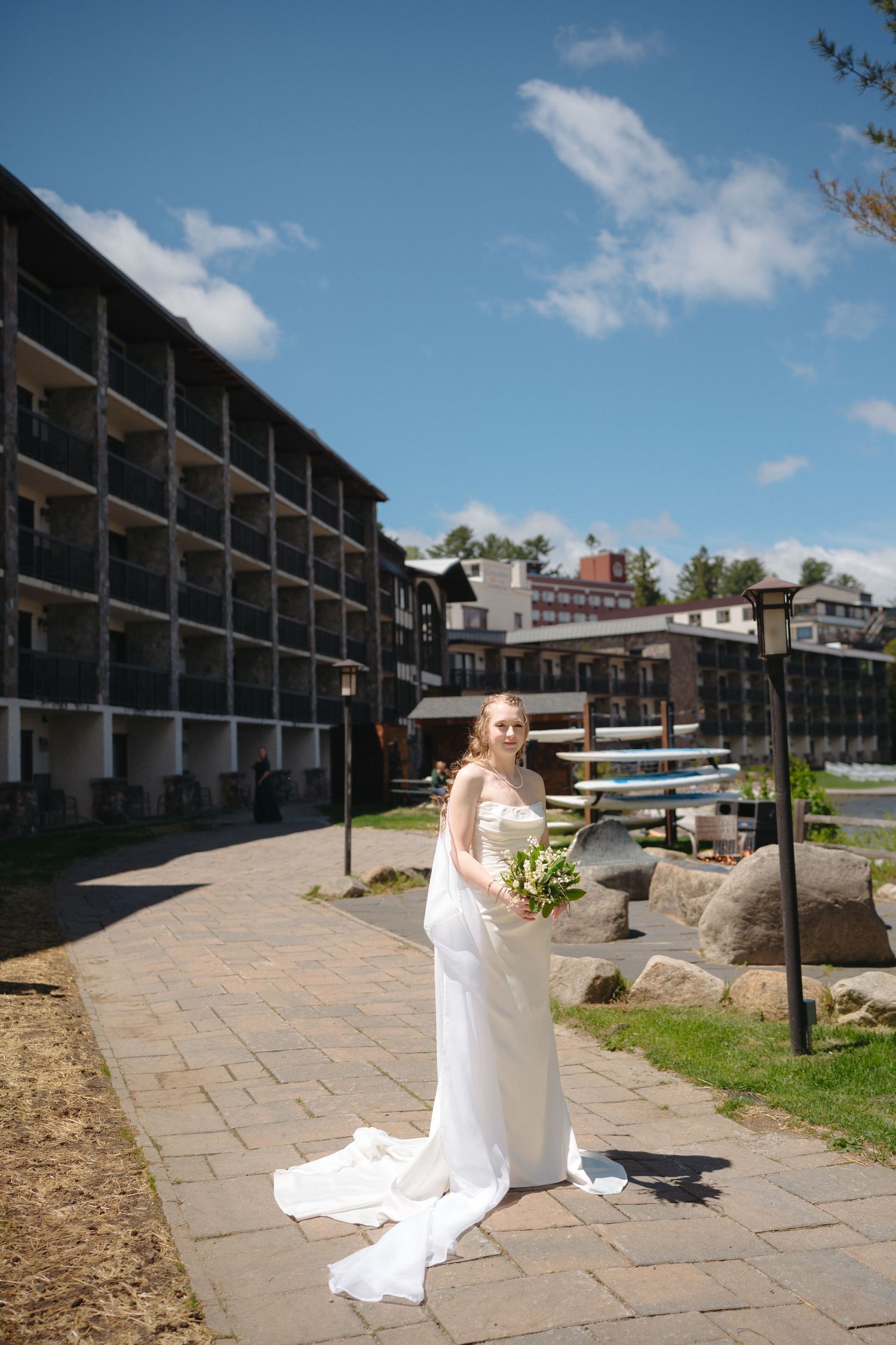 Bride in a white gown with a long train holds a bouquet outside a lakeside resort.
