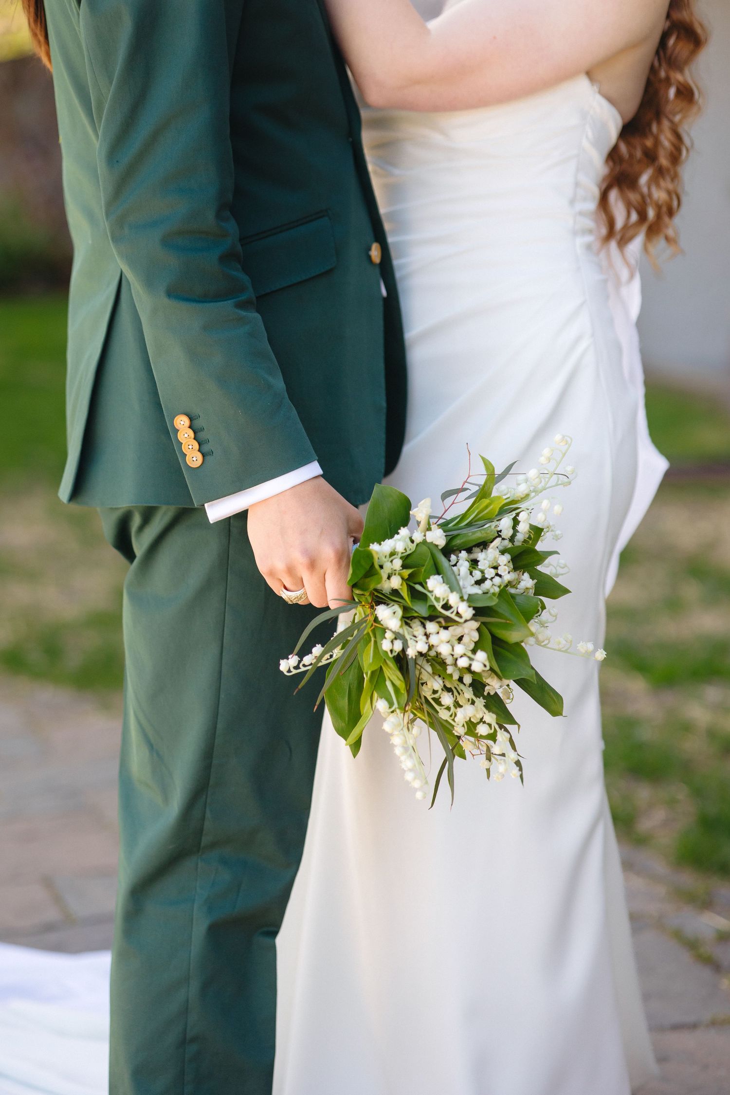 Bride and groom hold lily of the valley bouquet with greenery outdoors on wedding day.