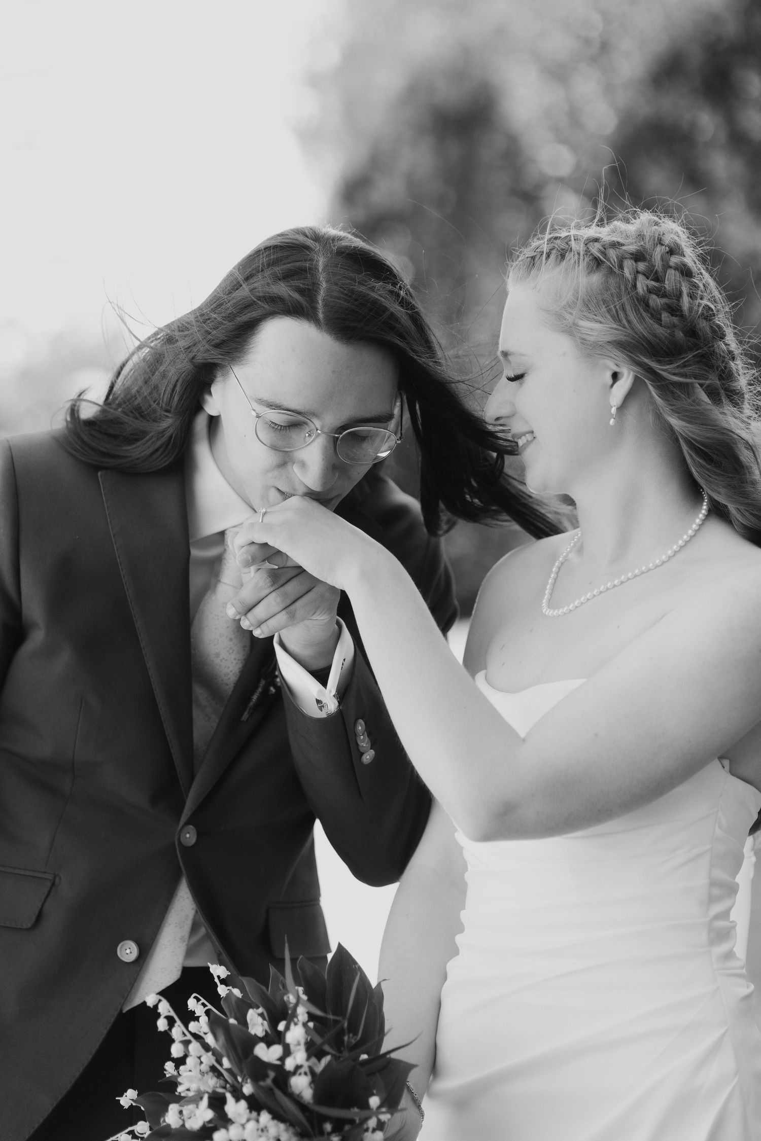 Black and white photo of groom kissing brides hand outdoors on their wedding day.