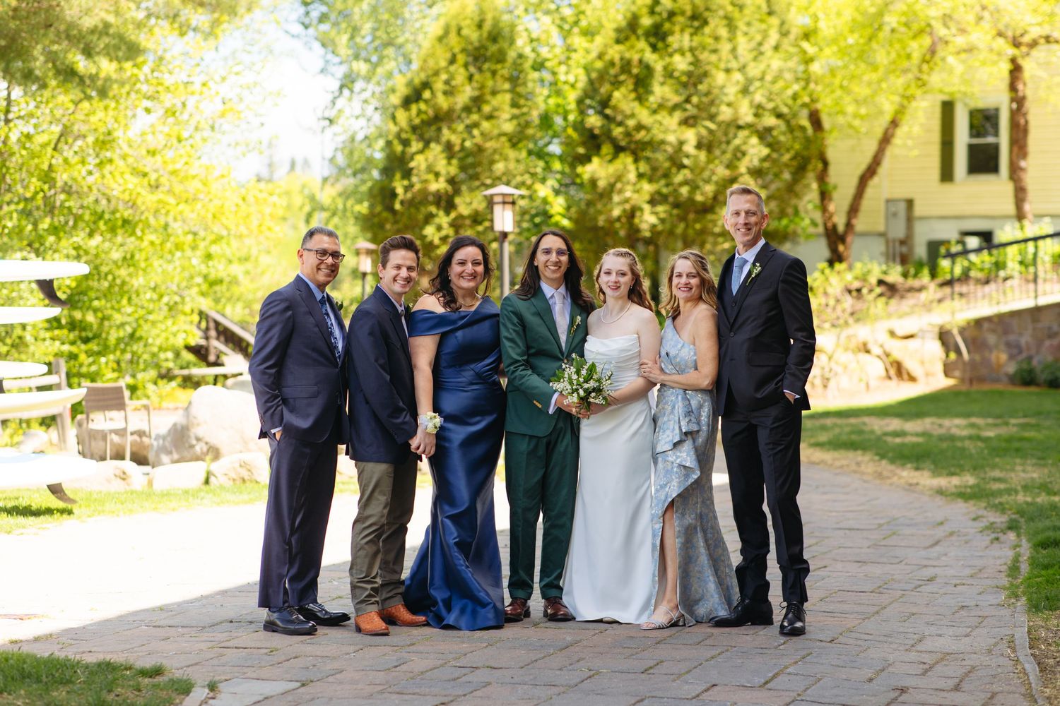 Wedding party of seven poses together on a stone path surrounded by lush green trees.