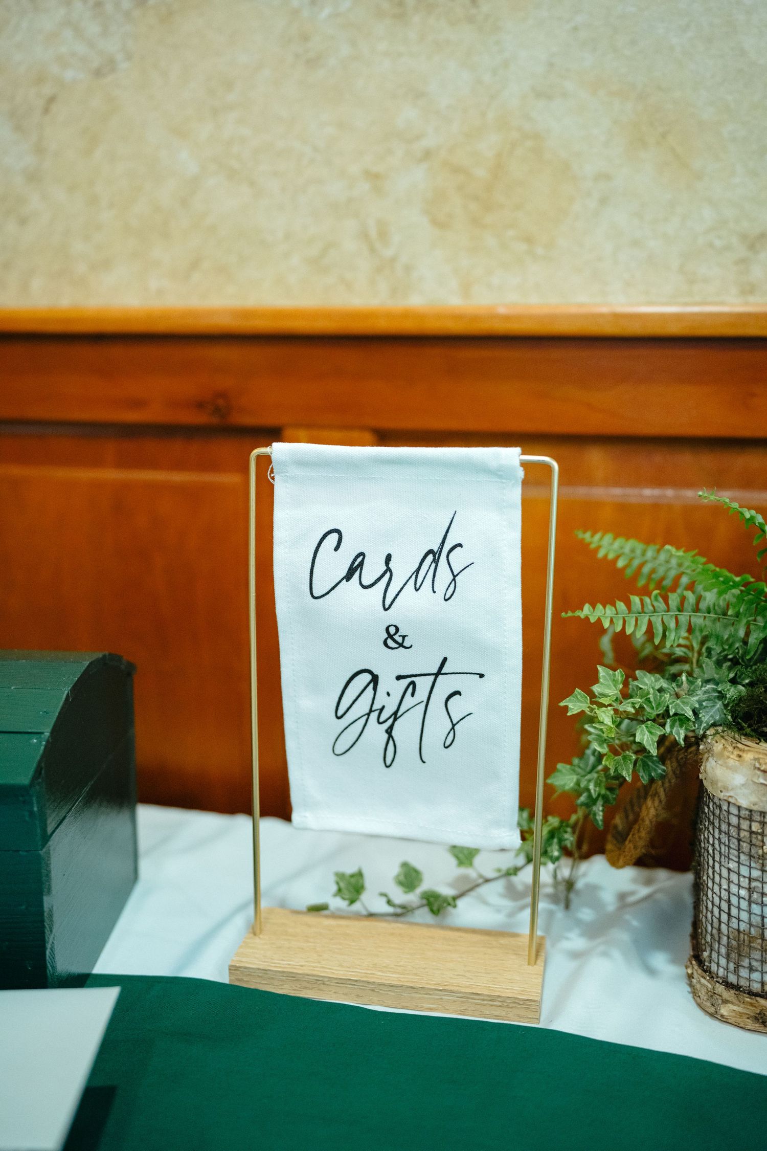 Elegant Cards and Gifts sign on a gold stand beside a green plant at a wedding reception table.