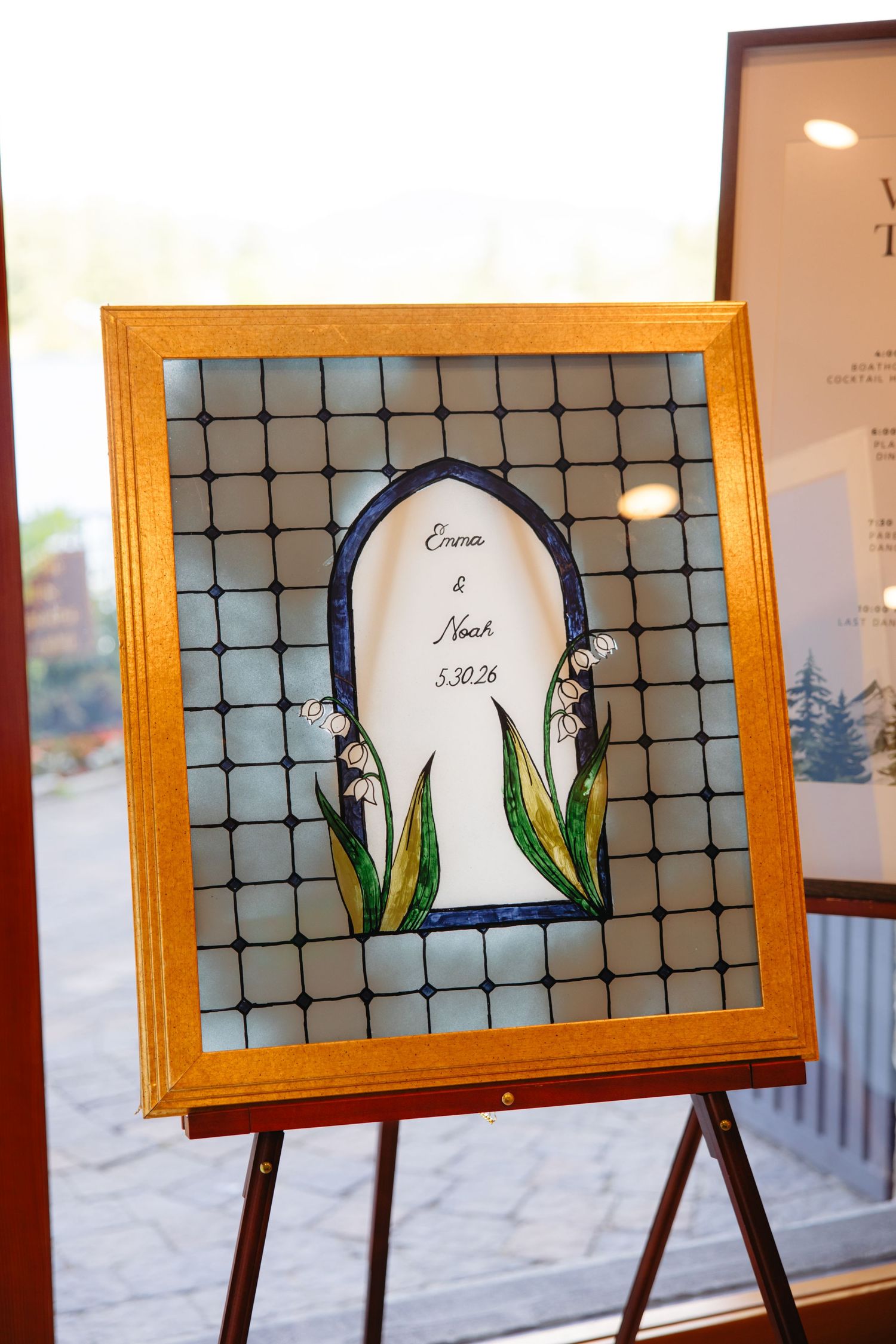 Stained glass wedding sign reading Emma and Noah 5.30.26 with lily of the valley design on easel.