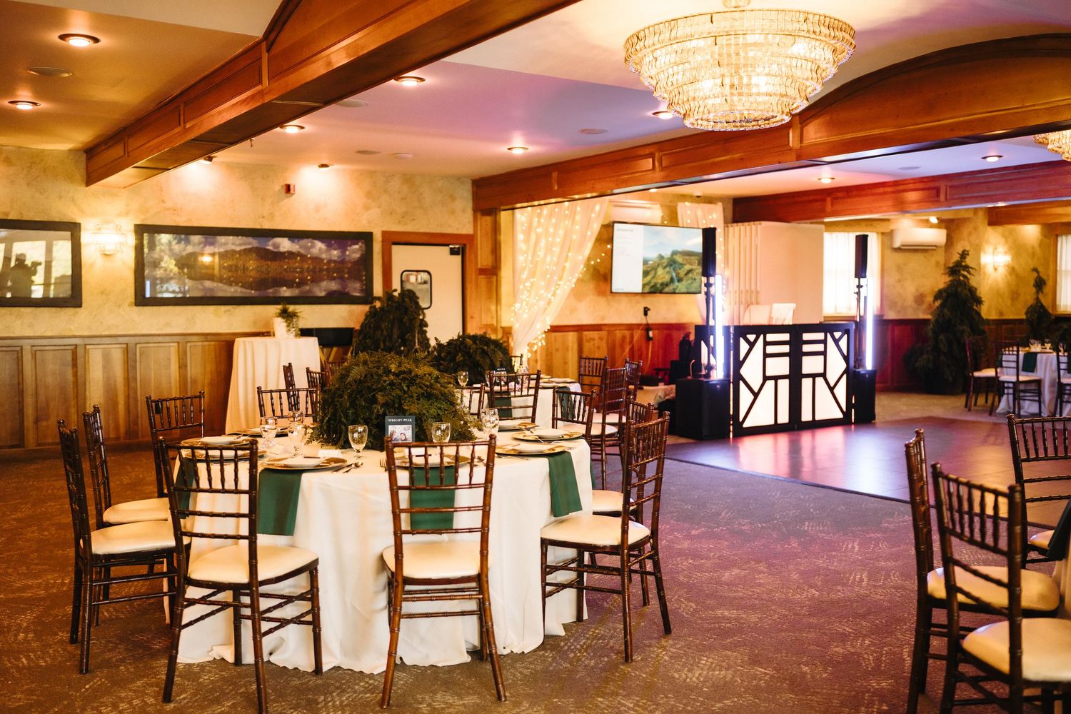 Elegant wedding reception venue with round tables, green linens, chiavari chairs, and a chandelier.