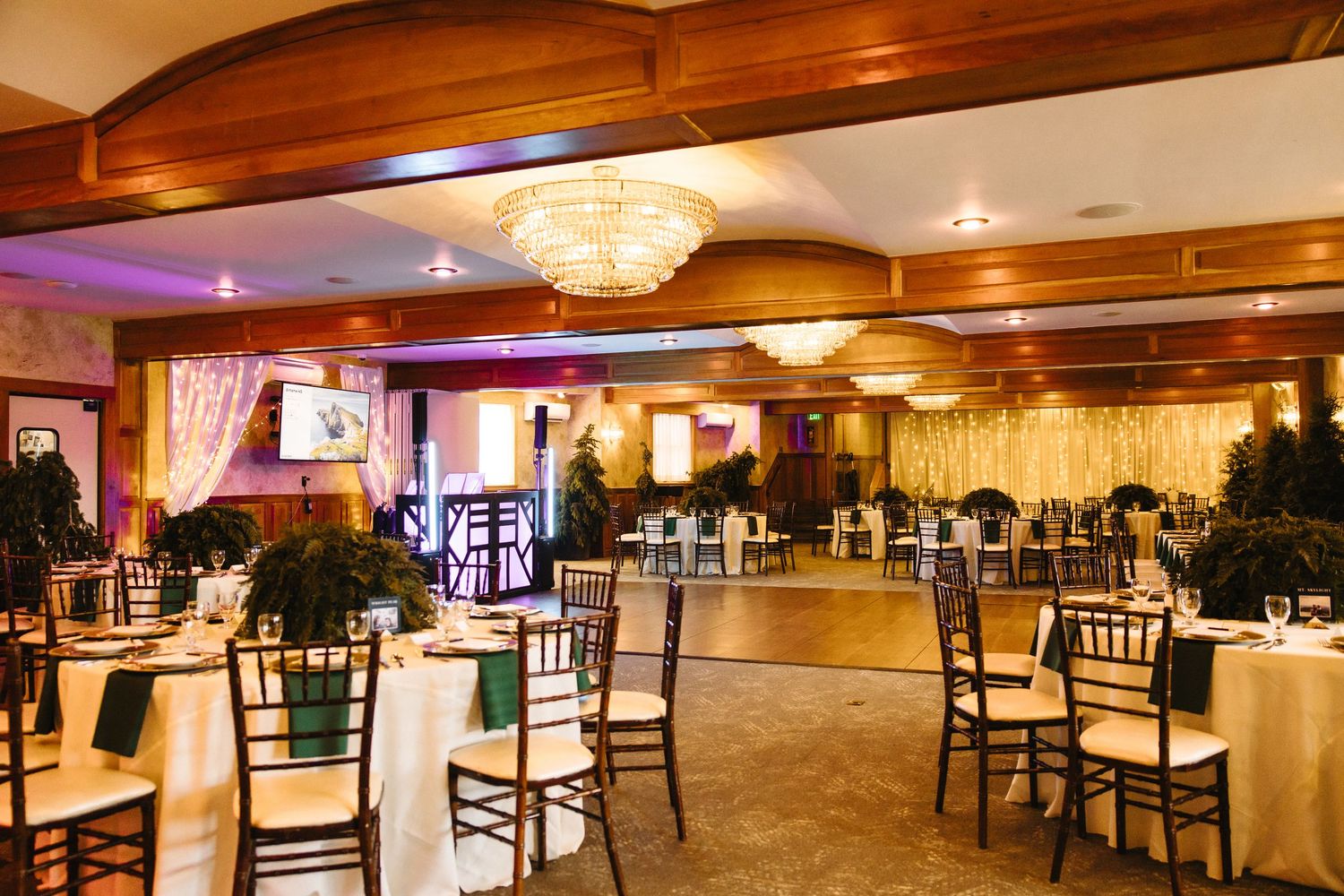 Spacious wedding reception hall with chandelier lighting, chiavari chairs, and dance floor.