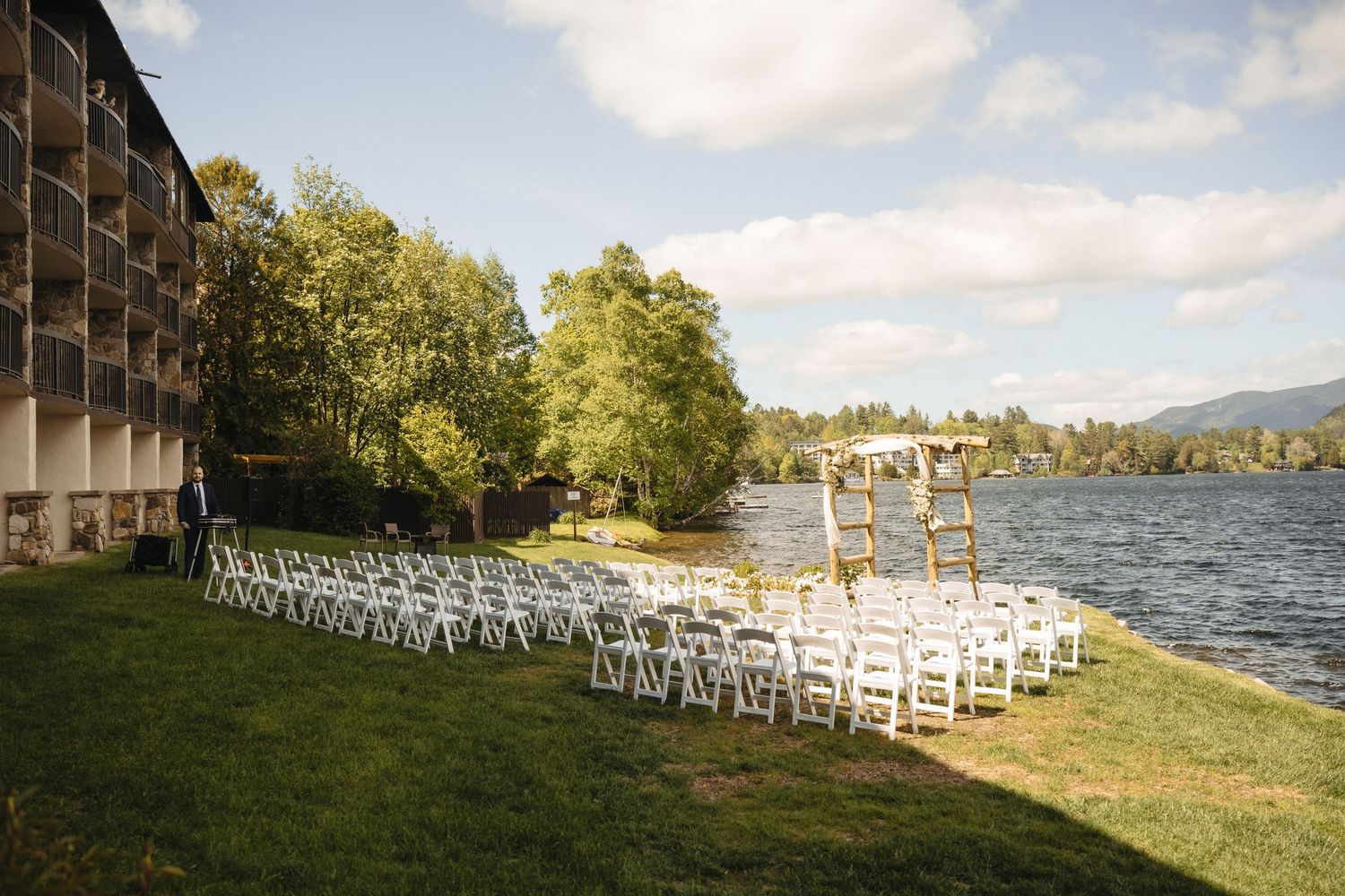 Elegant outdoor lakeside wedding ceremony setup with white chairs and floral arch by the water.