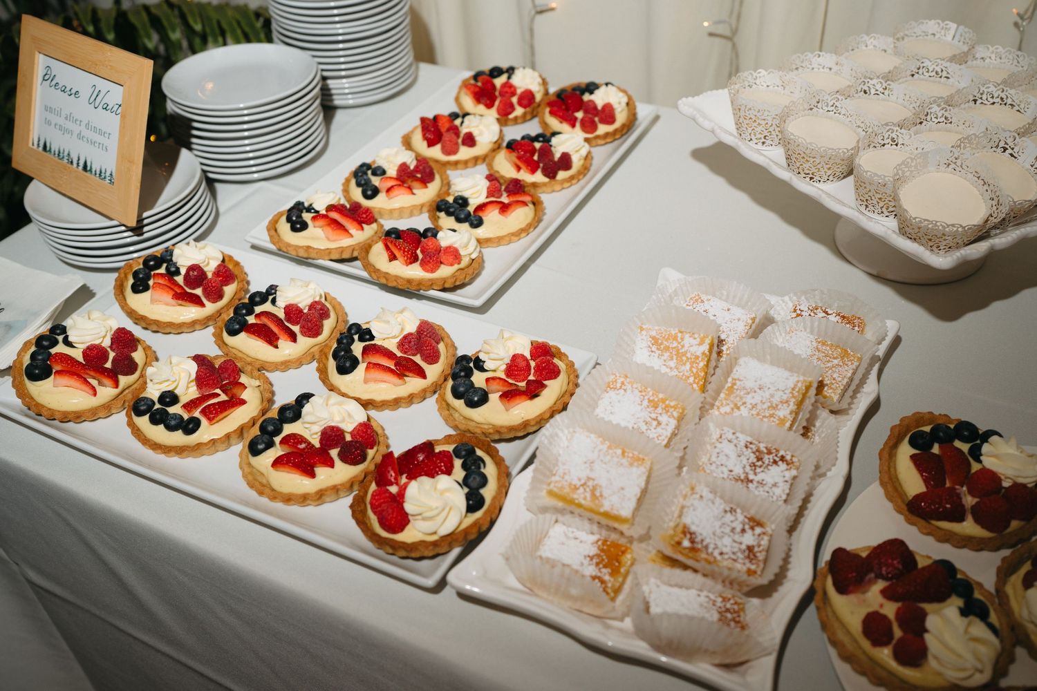 Elegant wedding dessert table with fruit tarts, powdered pastries, and berry topped treats.