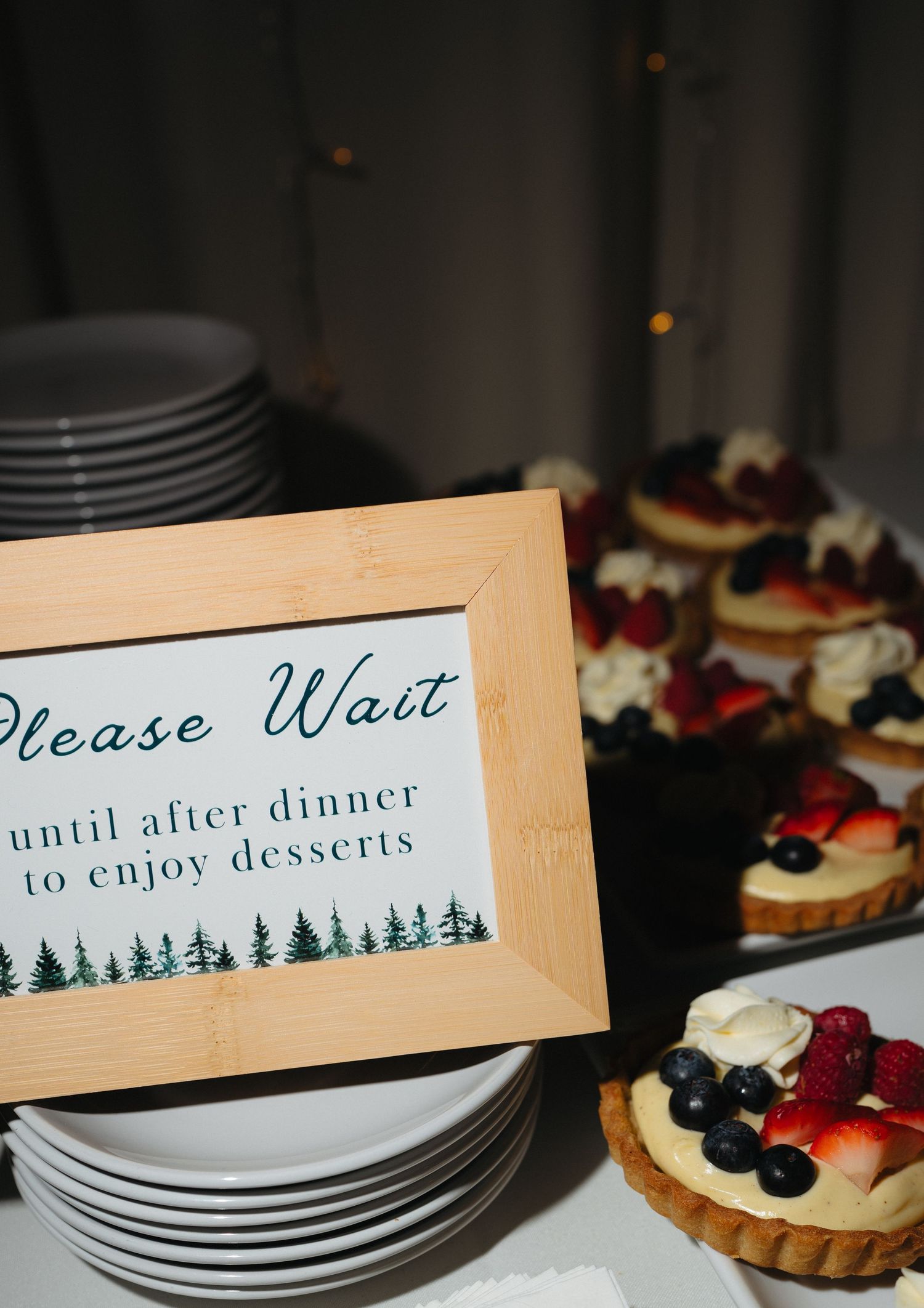 A dessert table with fruit tarts and a framed sign reading Please Wait until after dinner to enjoy desserts.