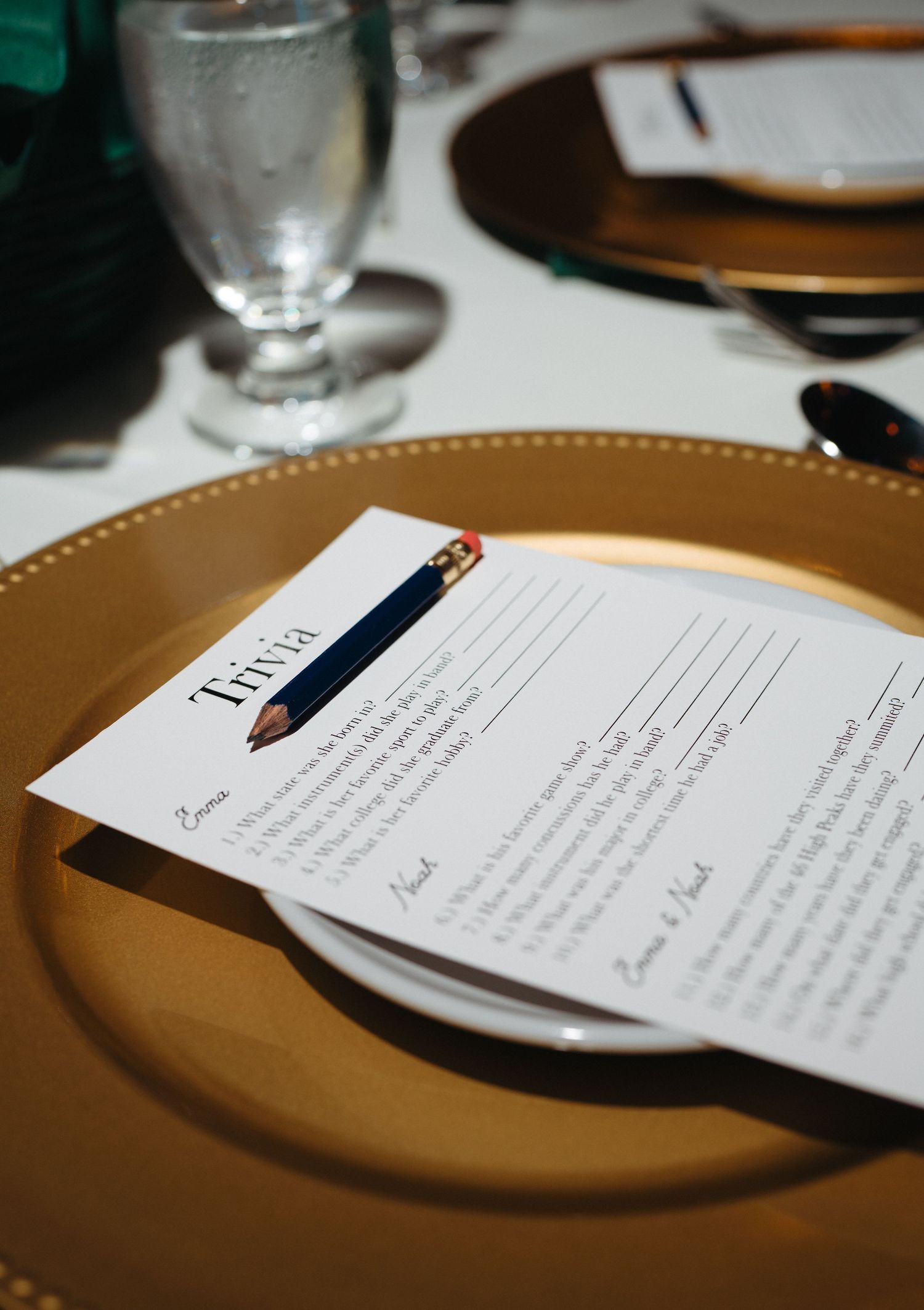 Gold charger plate with a trivia game card and pencil at a wedding reception table setting.