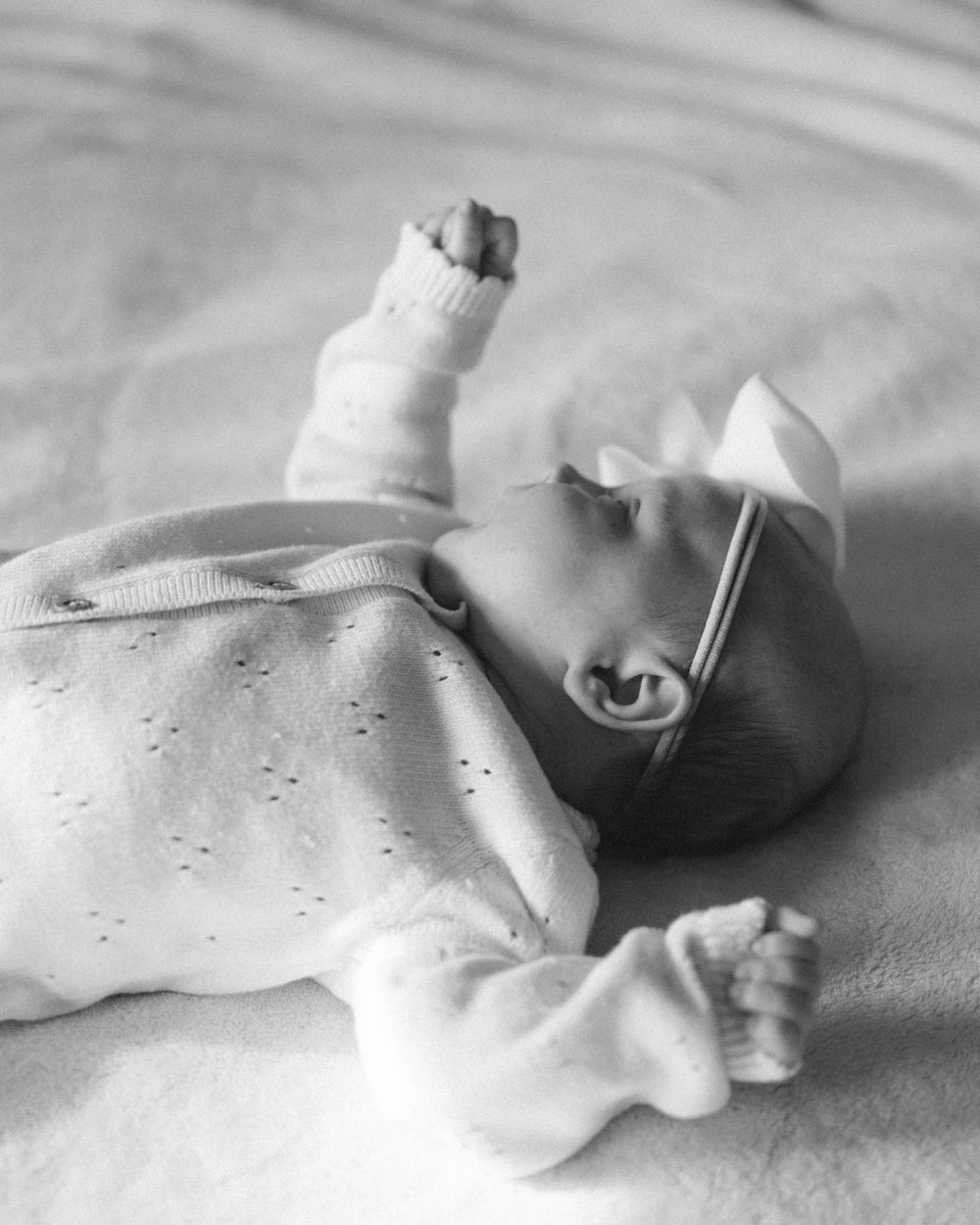 Black and white photo of peaceful newborn baby girl in dotted onesie with white bow headband.