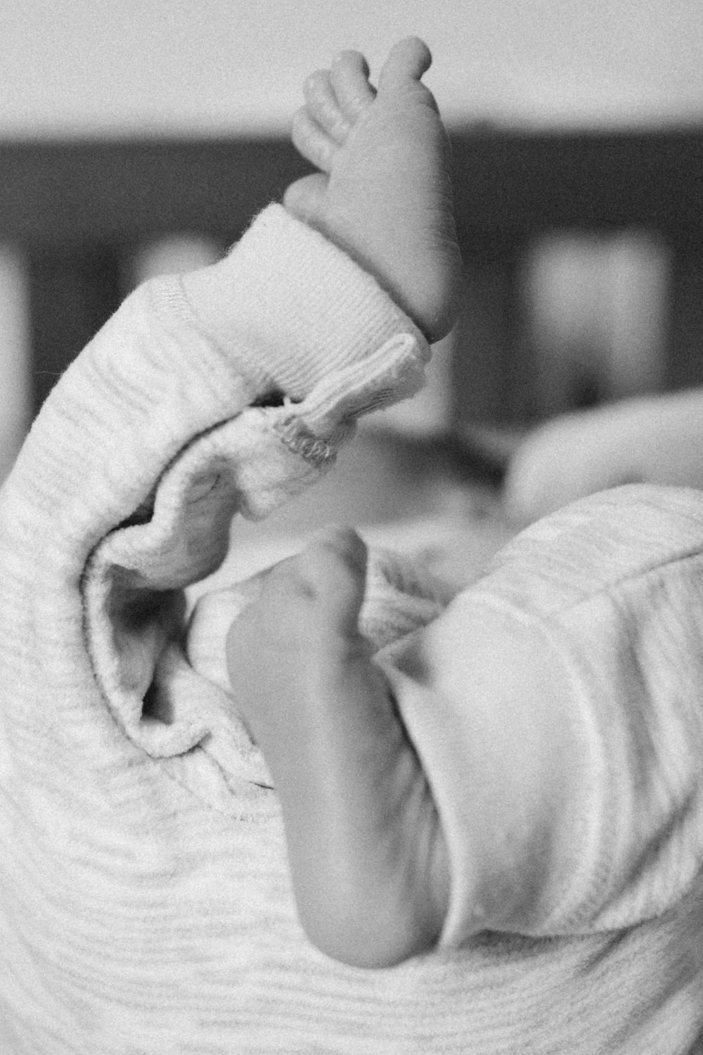Black and white close-up of newborn baby feet in striped onesie captured from above.