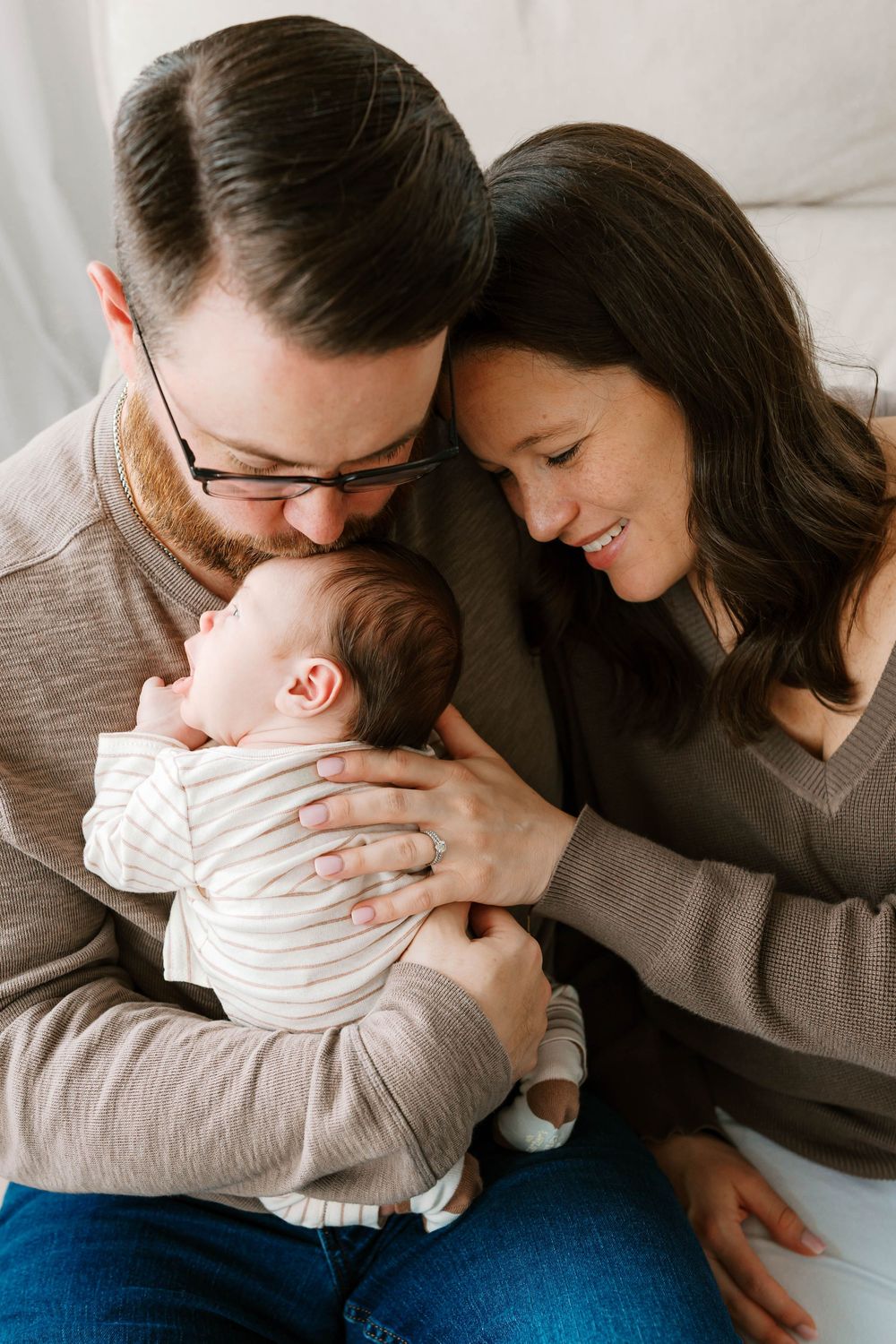 New parents lovingly cradle their sleeping newborn baby together in a warm, intimate family portrait.
