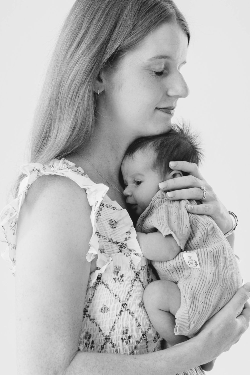 Black and white portrait of a mother tenderly holding her sleeping newborn baby close to her chest.