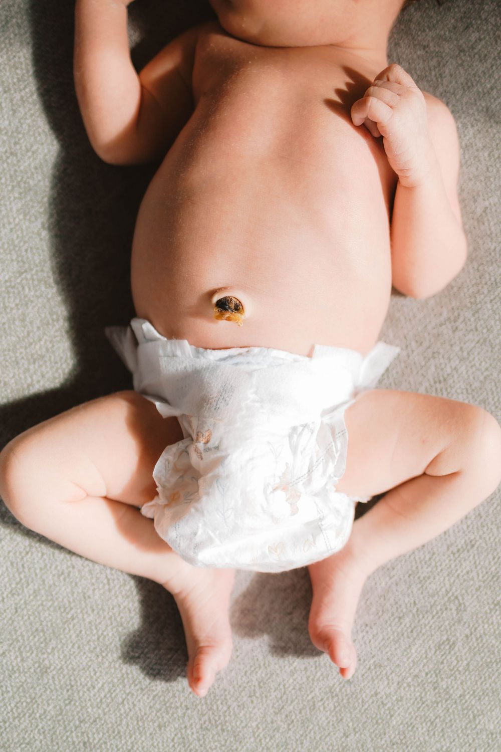 Overhead view of newborn baby in white diaper lying on a soft gray surface.