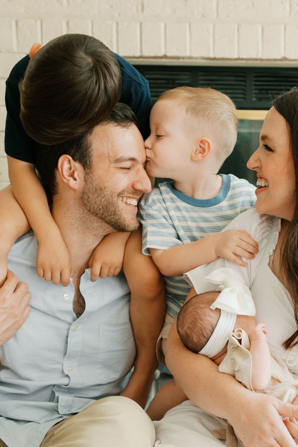 A happy family with two young boys and a newborn baby shares joyful kisses and hugs together.