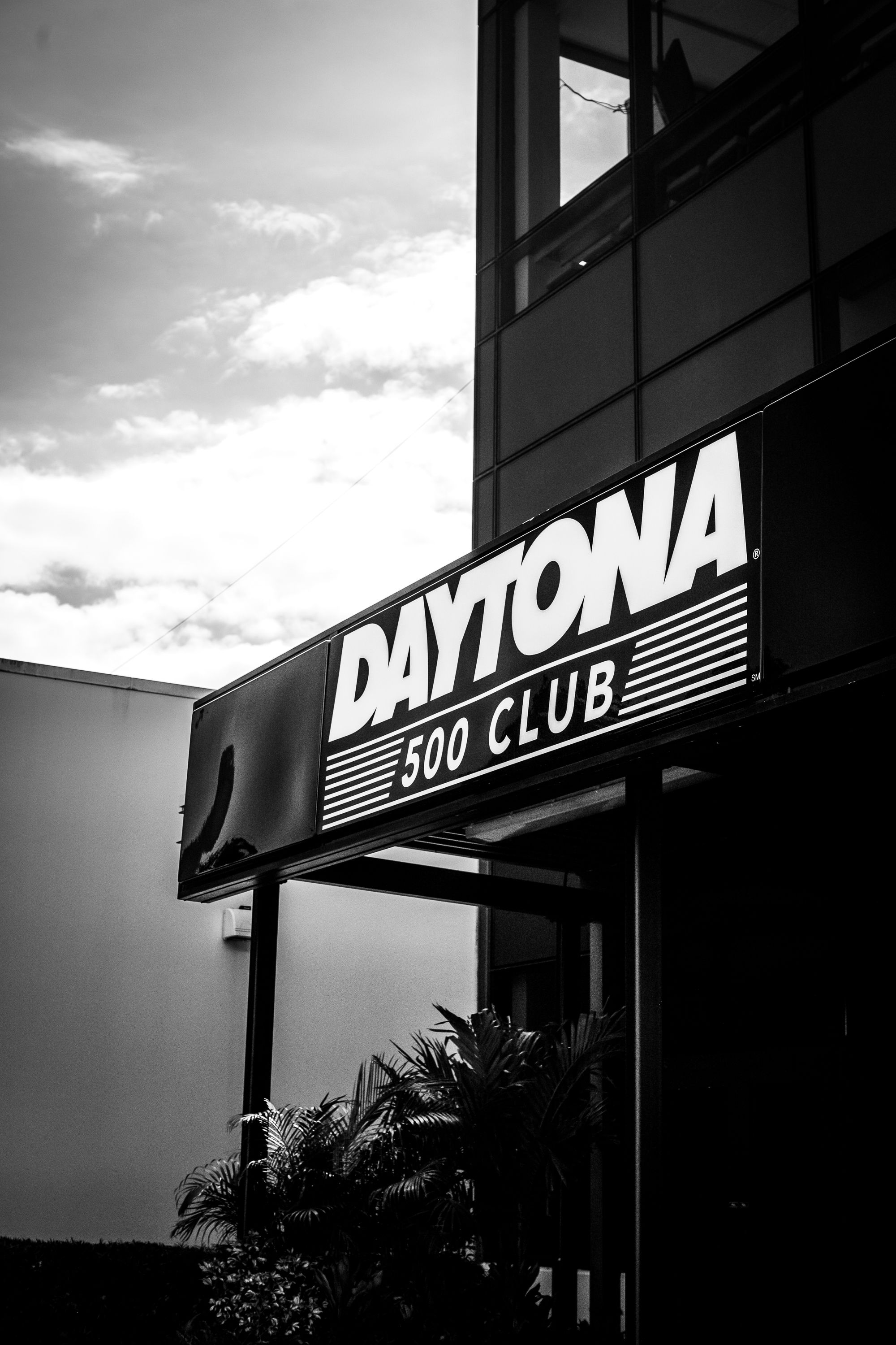 Black and white photo of the Daytona 500 Club sign on a building exterior with palm trees below.