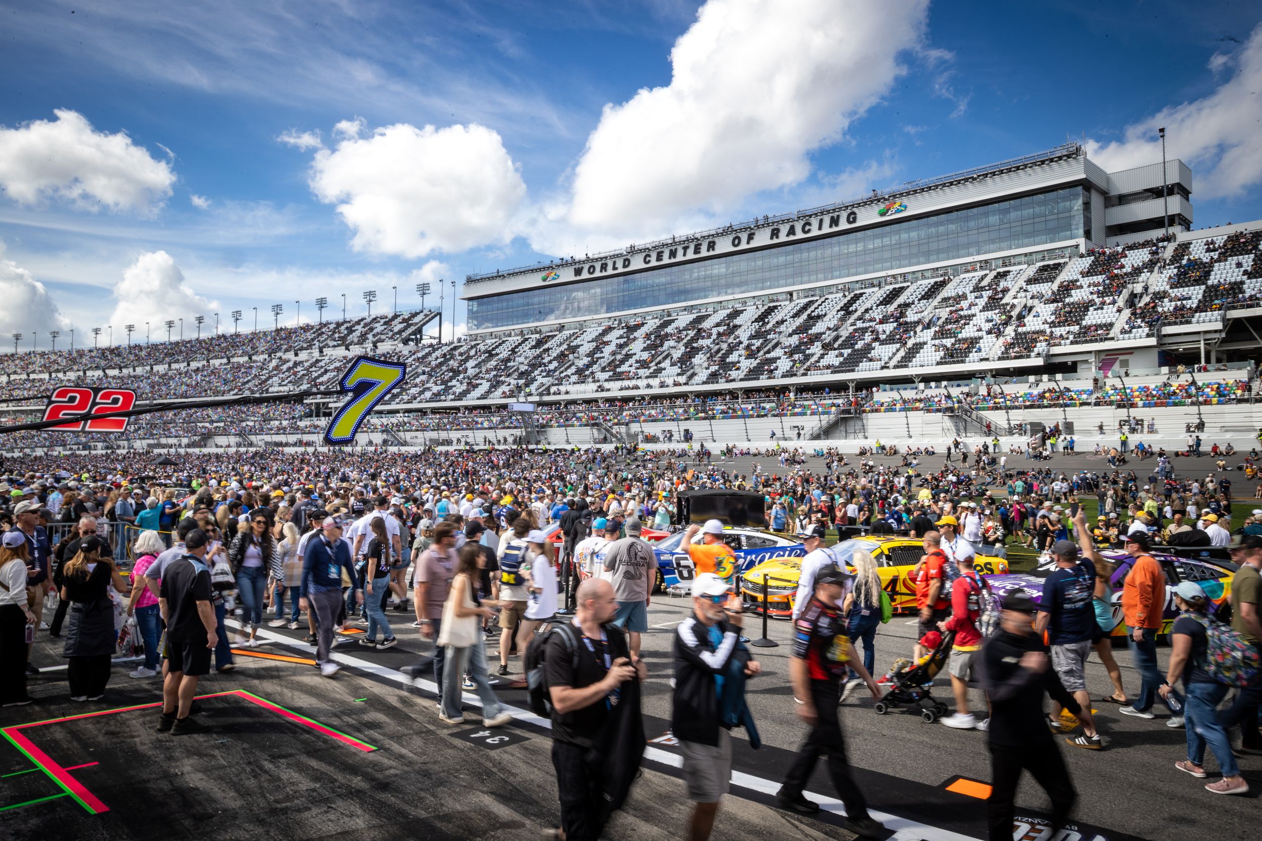 Crowds fill the pit lane at Daytona International Speedway during a NASCAR race day event with grandstands in background.