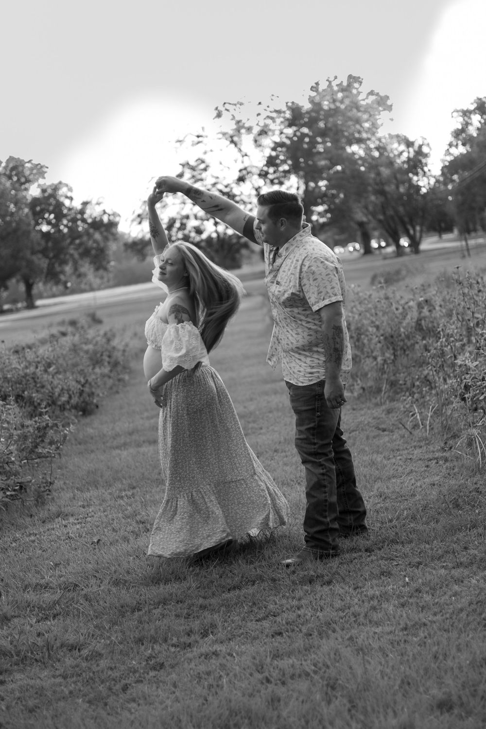 Expecting couple walking together through a field during a romantic outdoor maternity photography session, captured in black and white.