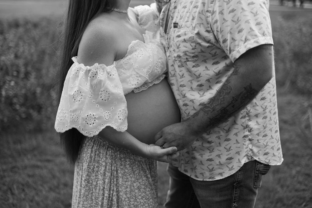 Expecting couple standing together outdoors as the father gently rests his hands on the mother's pregnant belly.