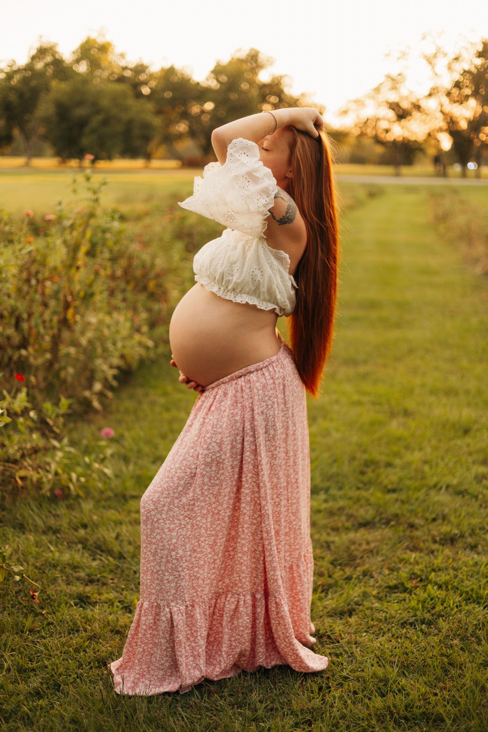 Pregnant mother posing sideways in a field during golden hour, highlighting her growing baby bump.