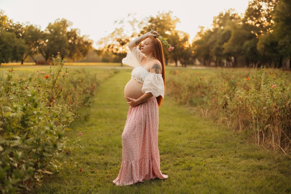 Expecting mother standing in a field surrounded by wildflowers during a warm outdoor maternity photography session.