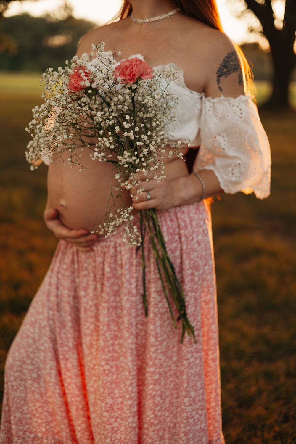 Pregnant mother holding a bouquet of pink and white flowers while posing outdoors during a golden-hour maternity photography session.Pregnan