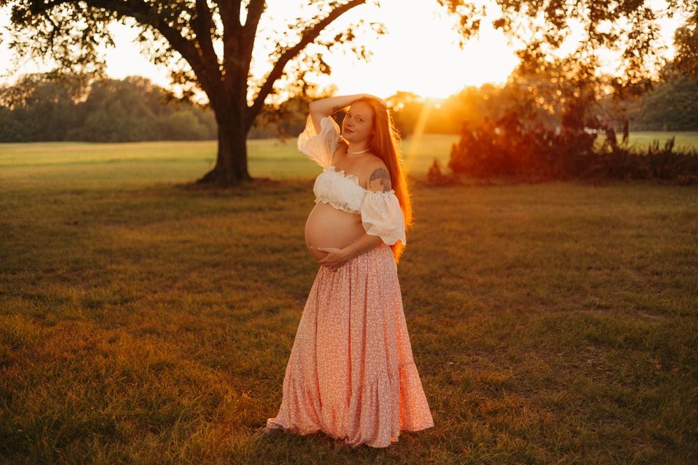 Pregnant mother posing in a field at sunset during a warm, romantic outdoor maternity photography session.