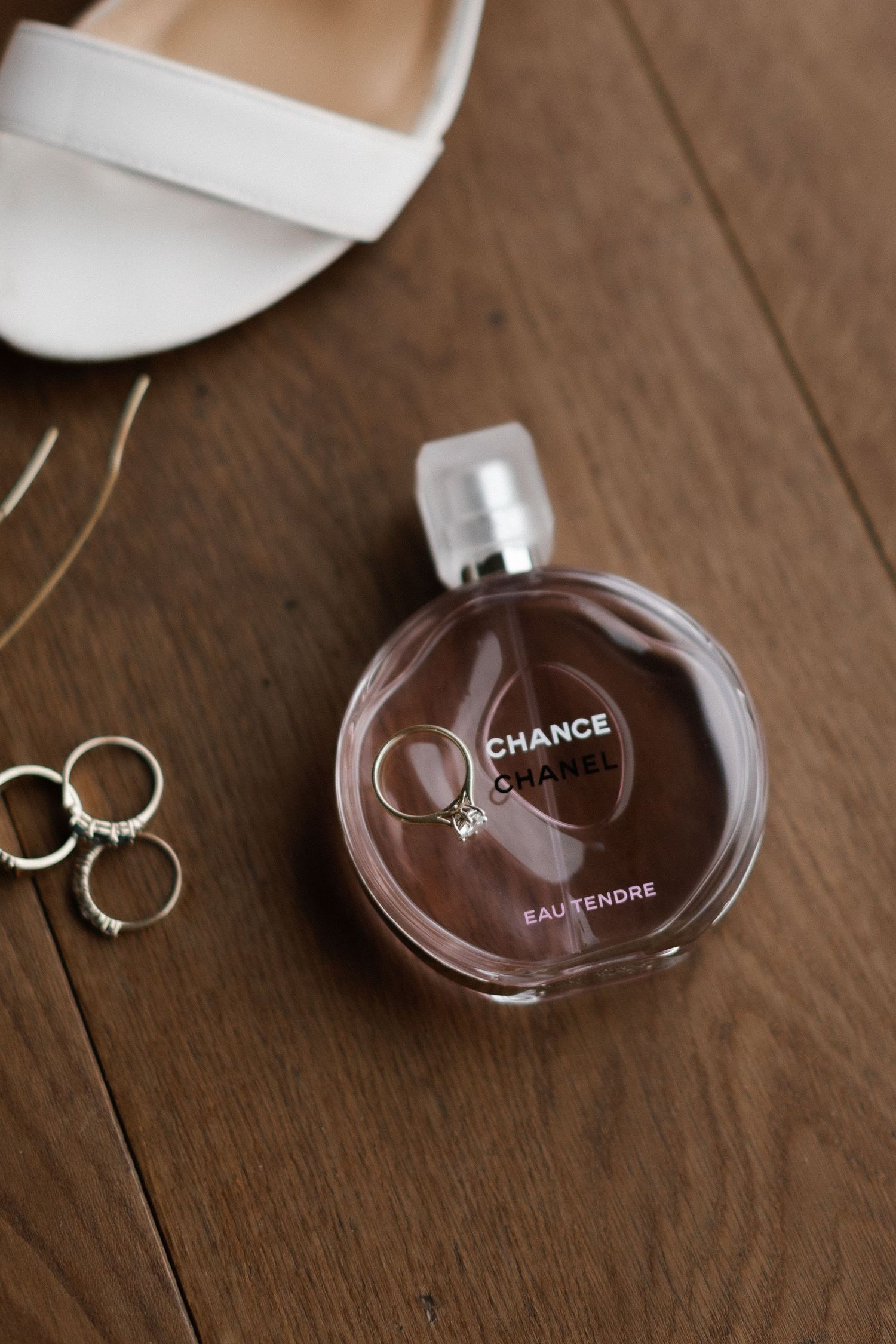 Chanel Chance Eau Tendre perfume bottle with wedding rings and white bridal heels on wooden floor.