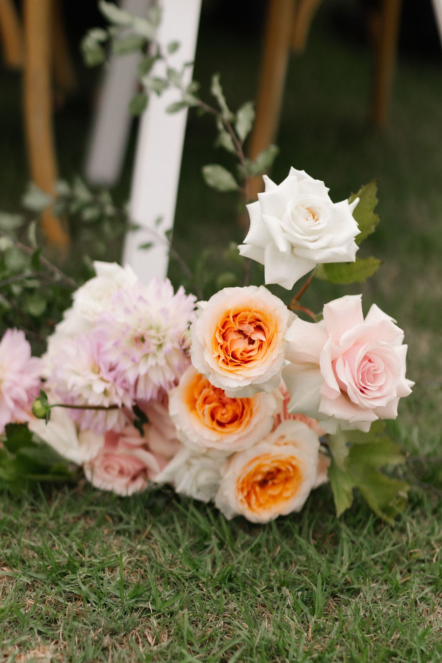 Wedding bouquet of peach, pink and white roses resting on green grass.