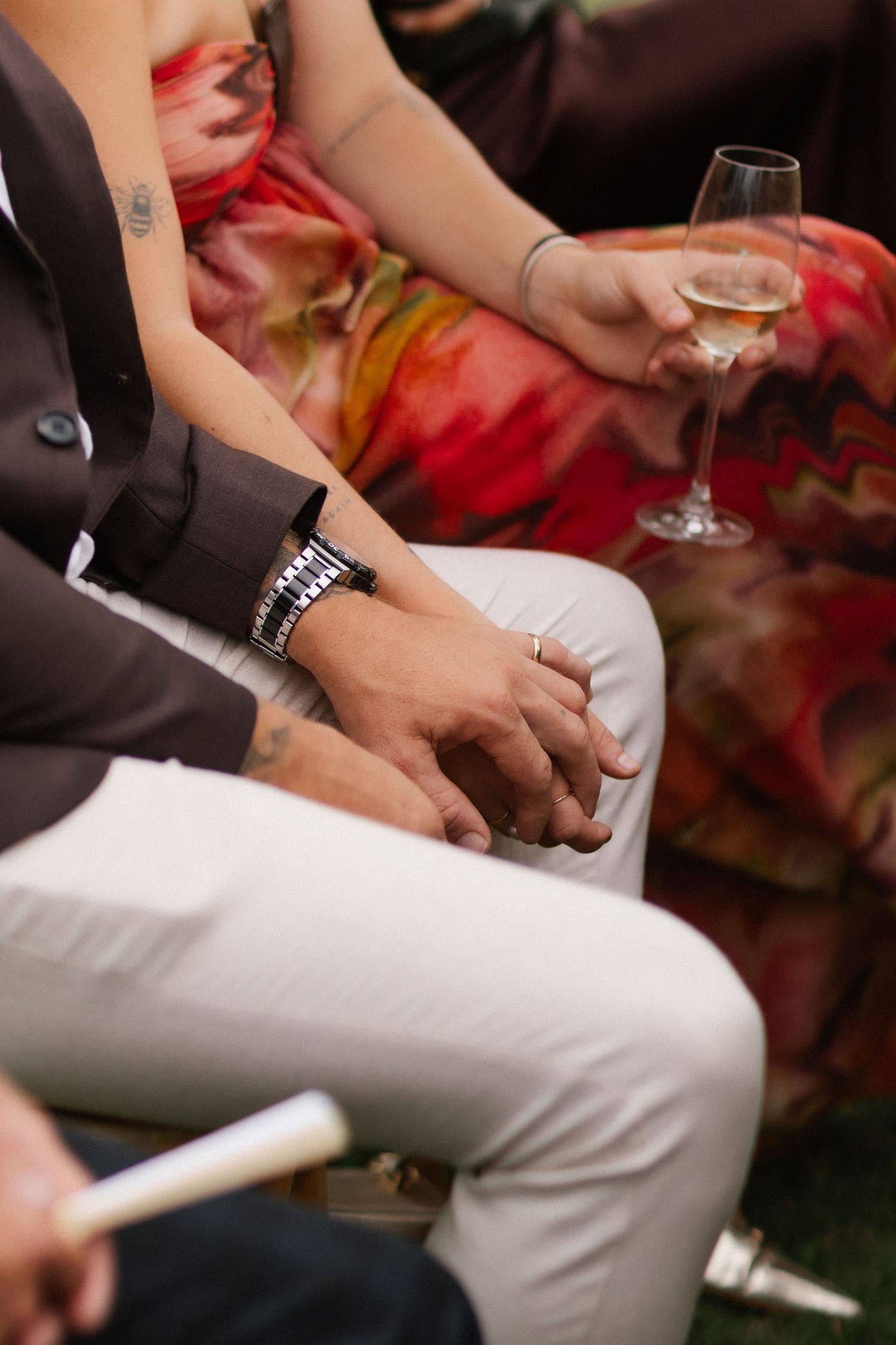 Couple holding hands at wedding reception, woman holding champagne glass, man wearing watch.