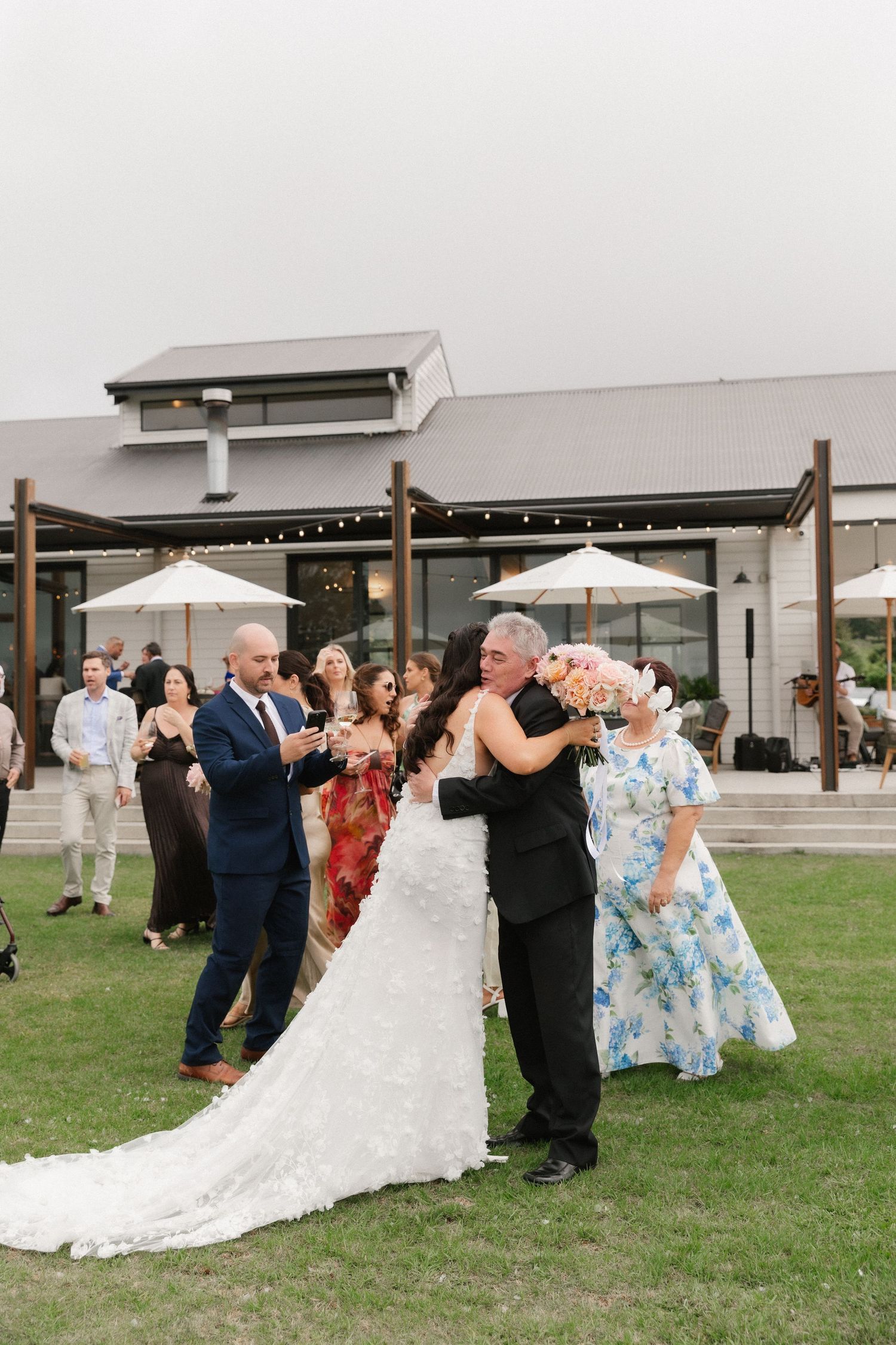 Bride in white gown embracing family member during outdoor wedding reception at elegant venue.
