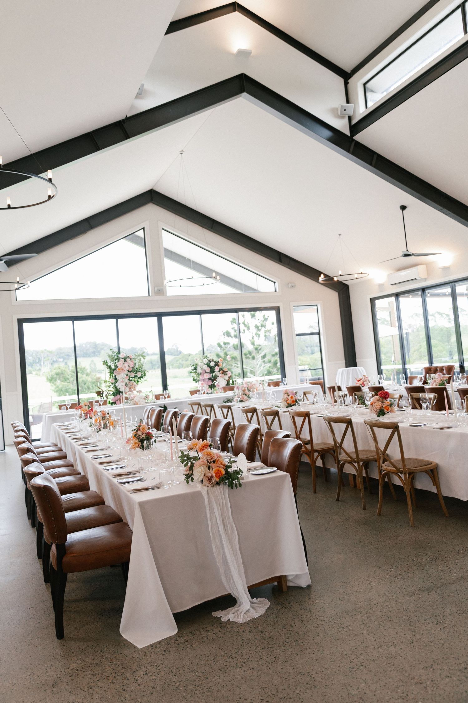 Elegant wedding reception hall with vaulted ceilings, long white tables, and floral centerpieces.