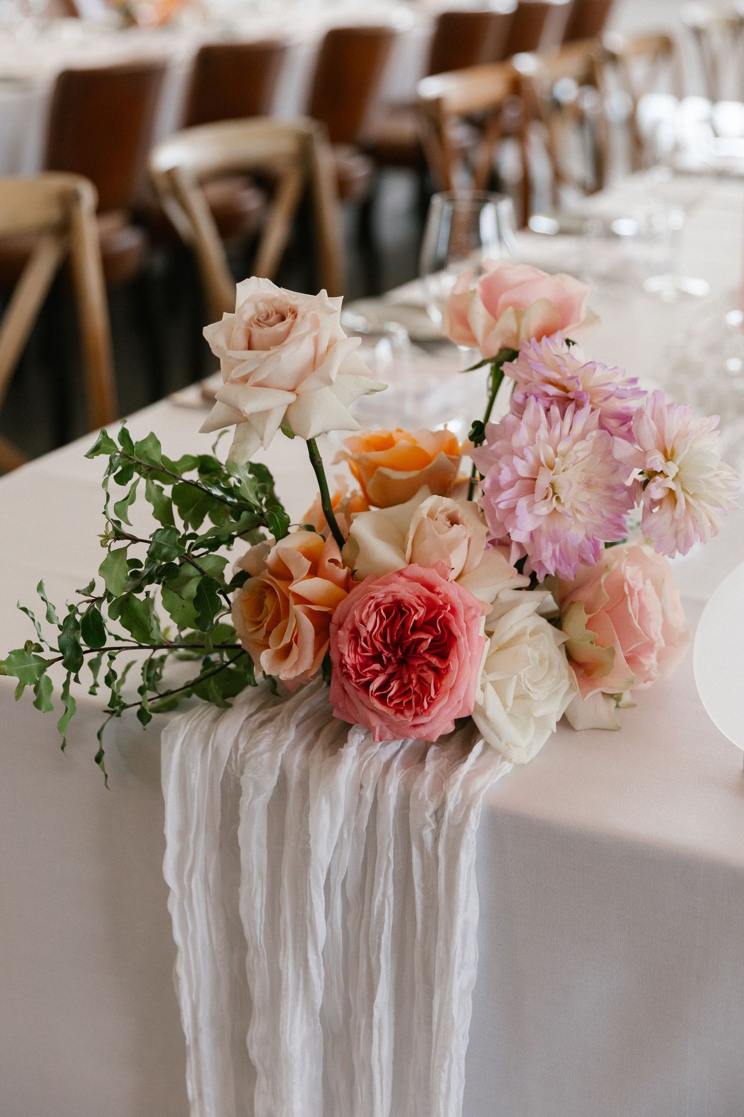 Elegant wedding table centerpiece featuring pink, peach, and white roses on a white linen runner.