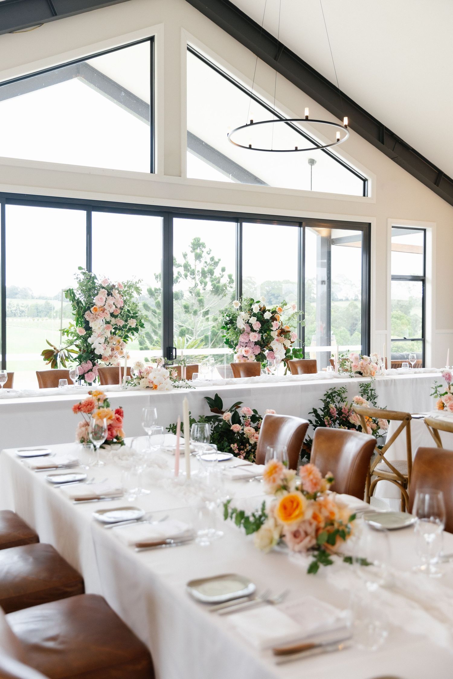Bright modern wedding reception venue with high ceilings, large windows, and pink floral centerpieces.
