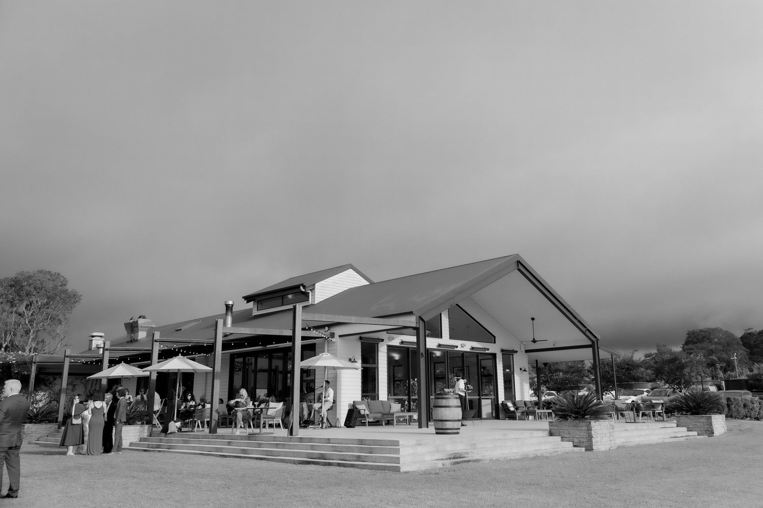 Black and white exterior photo of a rustic wedding venue under dramatic cloudy sky.